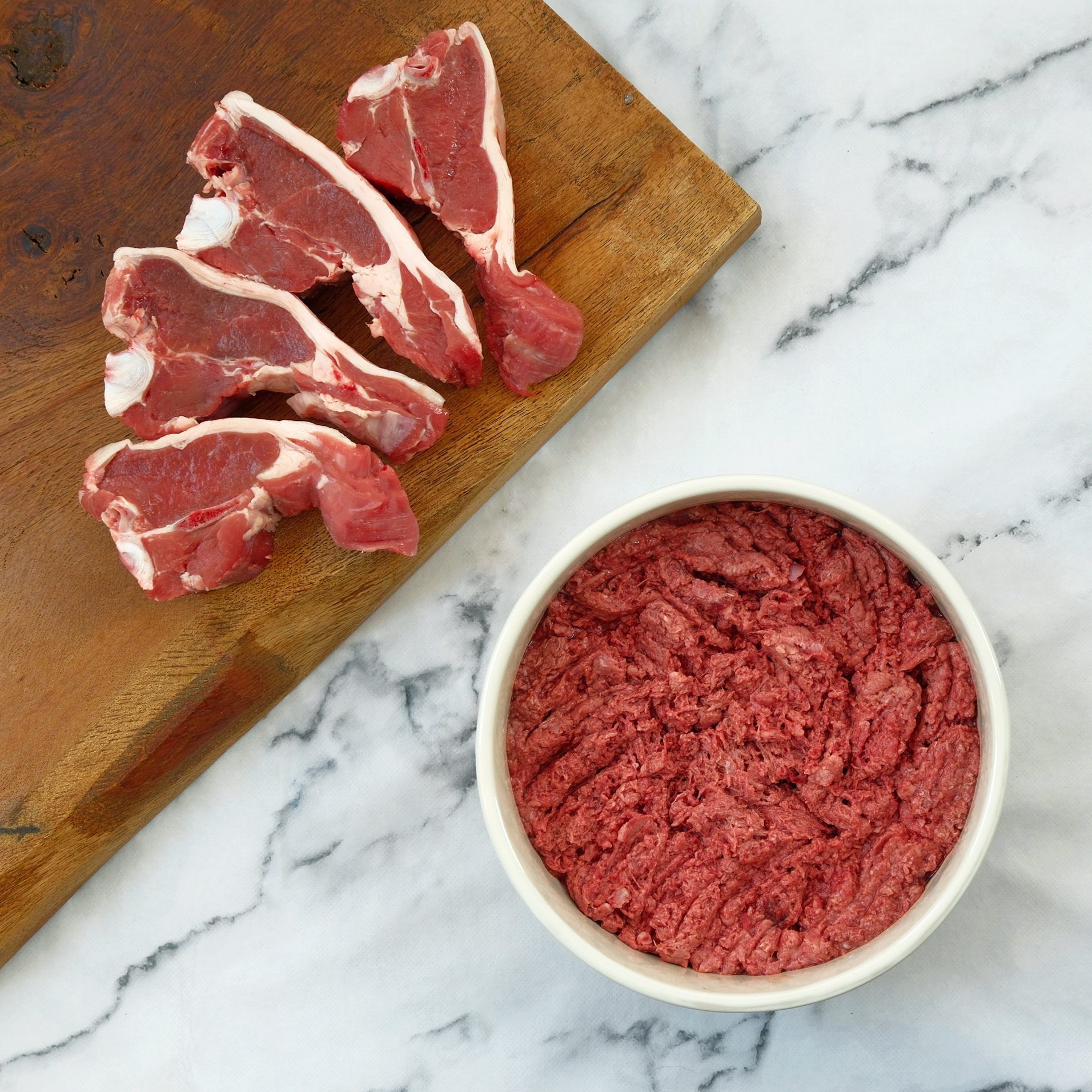 Raw lamb chops and ground lamb in a white bowl on a wooden board.
