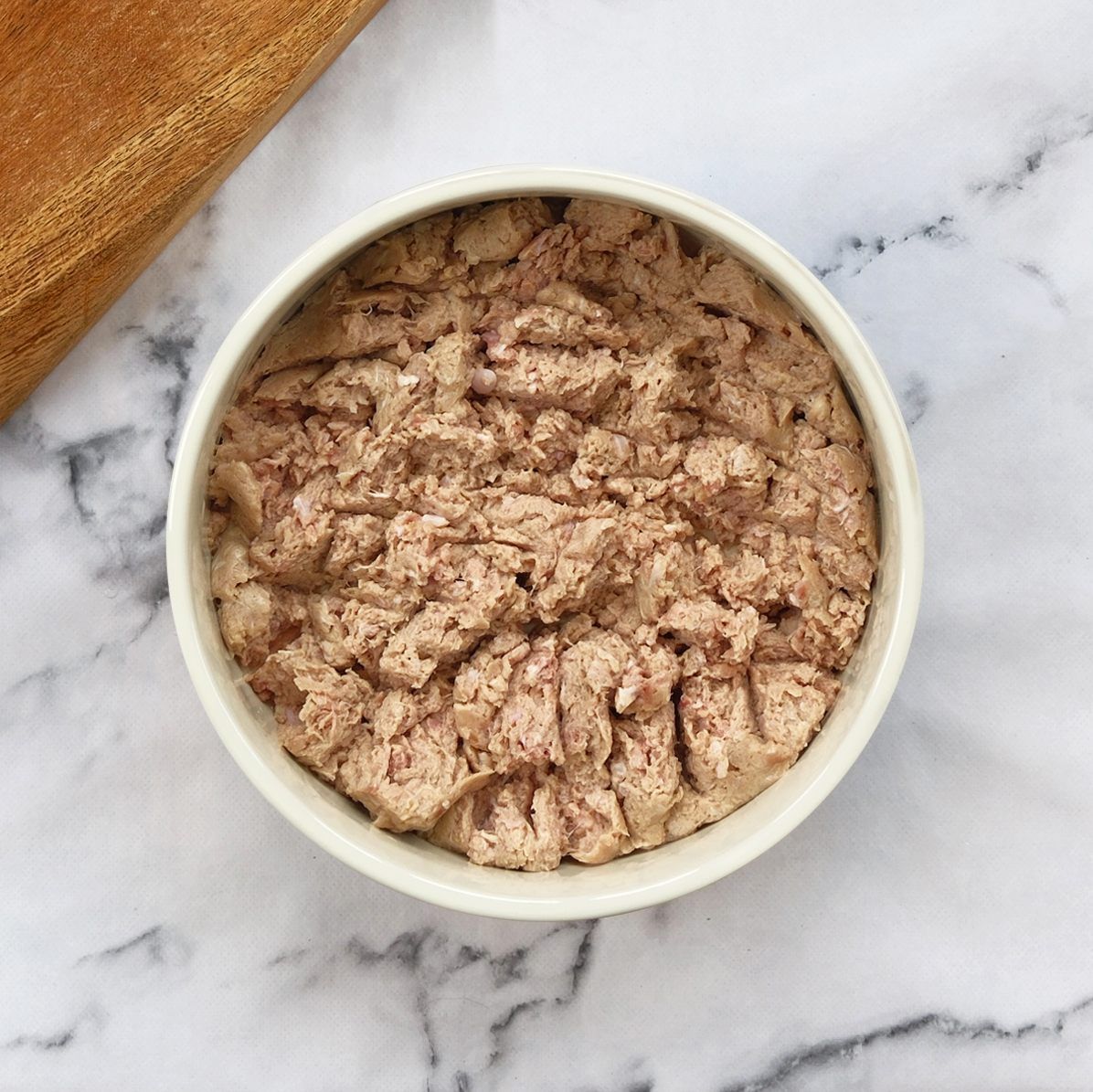 Close-up of a white bowl filled with light brown pâté on a marble surface.