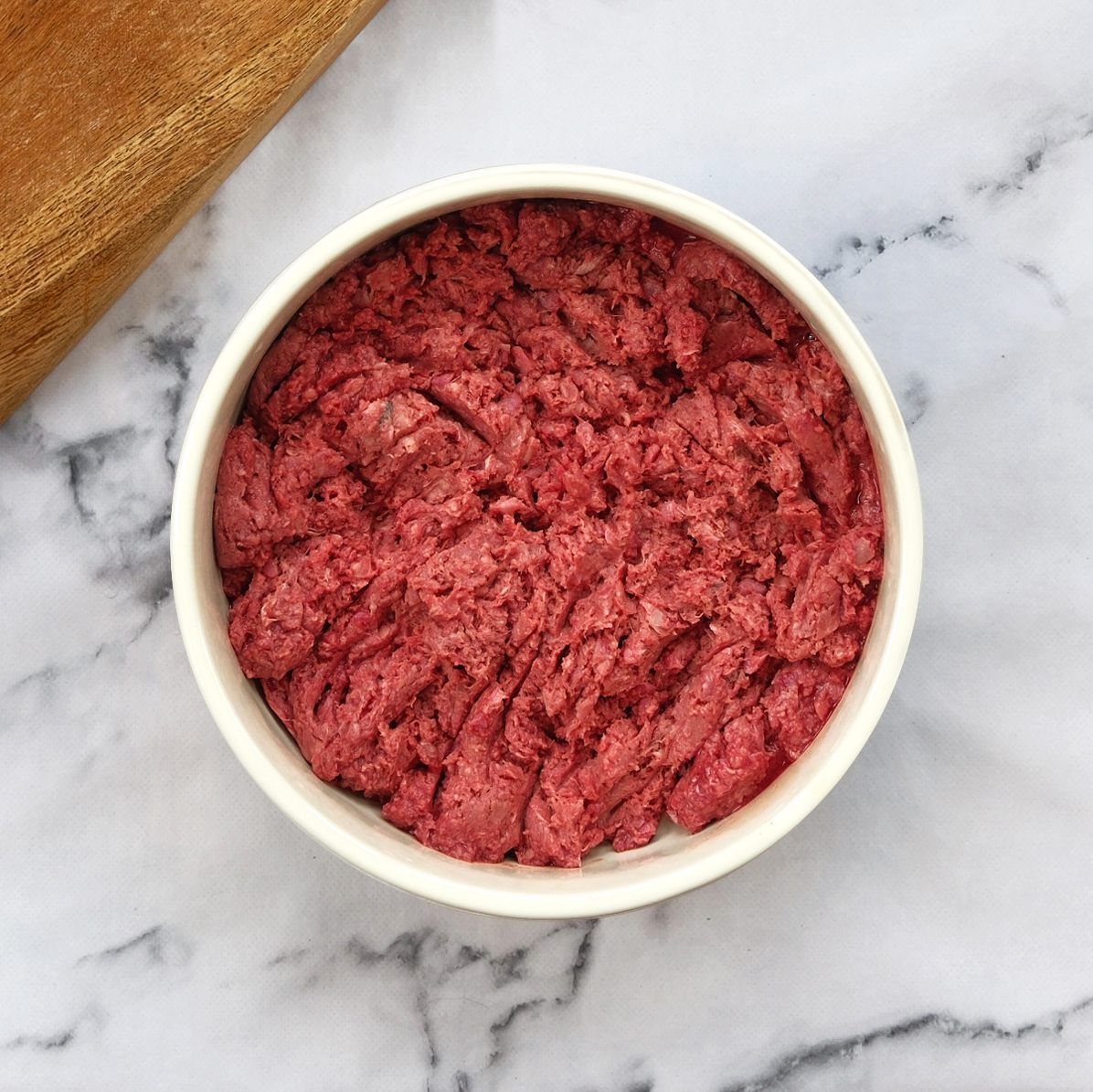 Bowl of ground red meat, possibly for pets, on a marble surface.