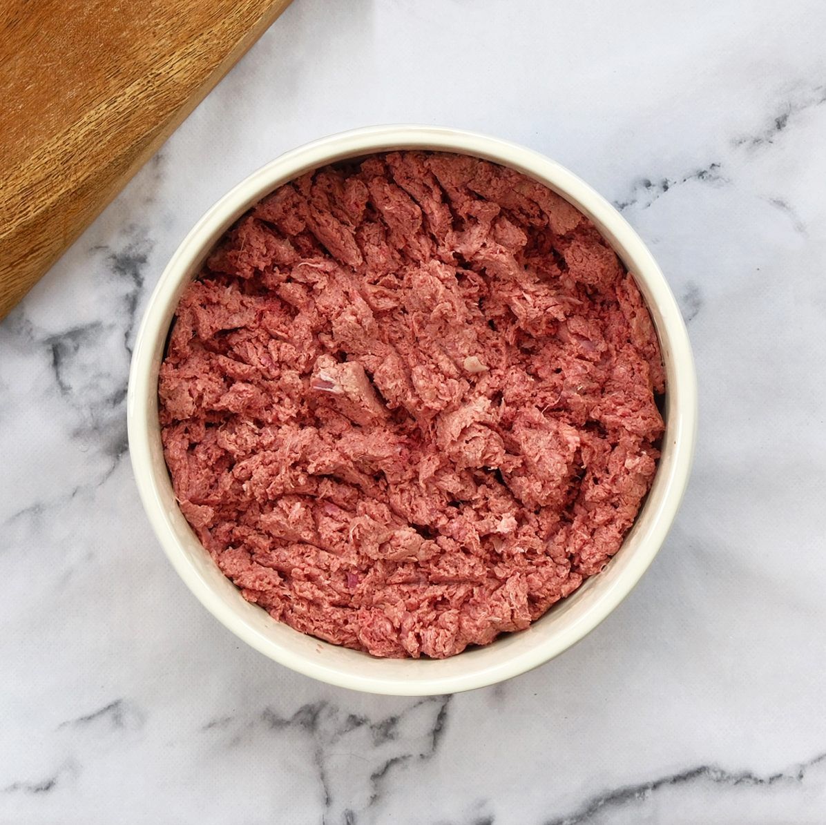 Bowl of pink food on a marble surface, next to a wooden cutting board.