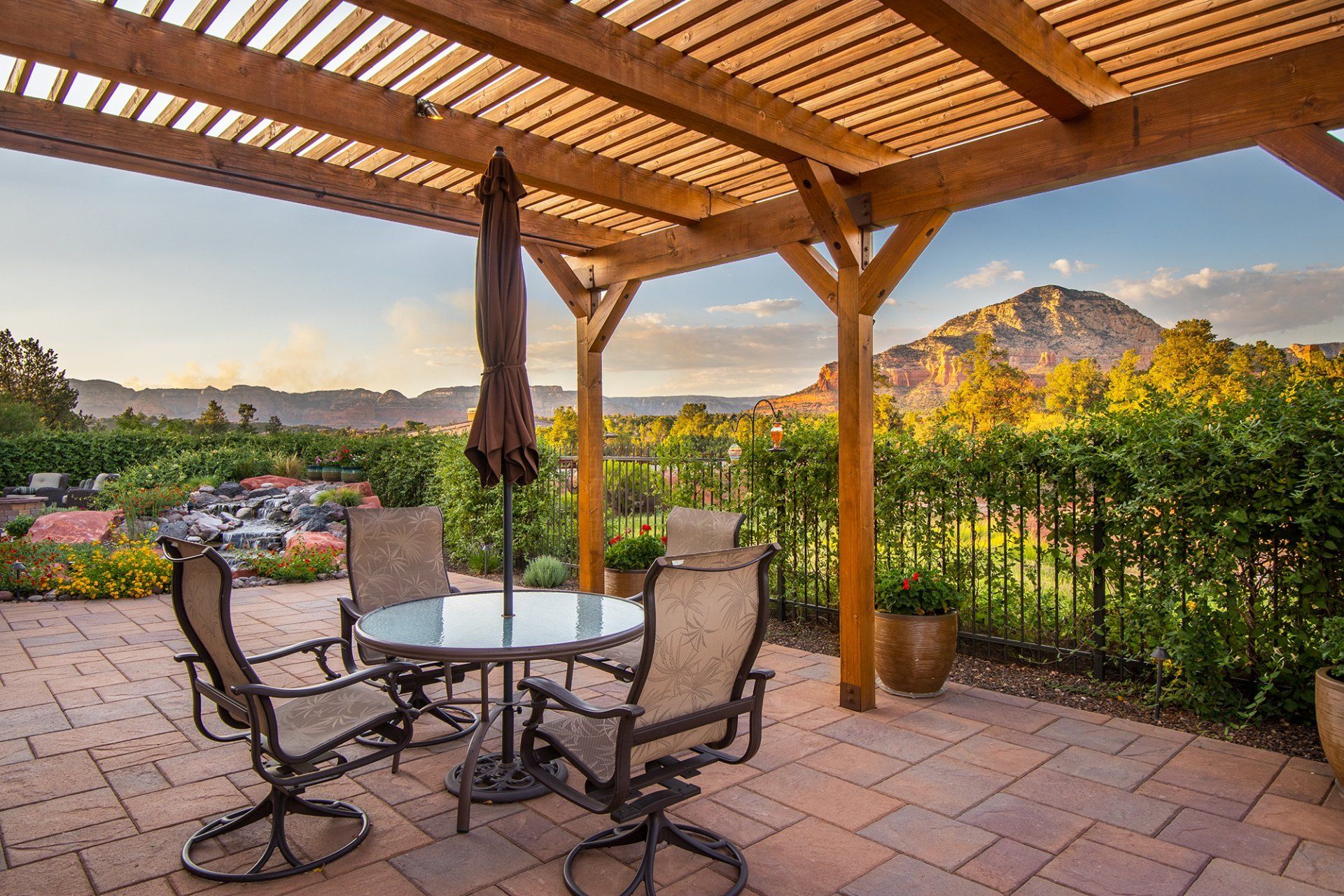 A patio with a table and chairs under a pergola with mountains in the background.