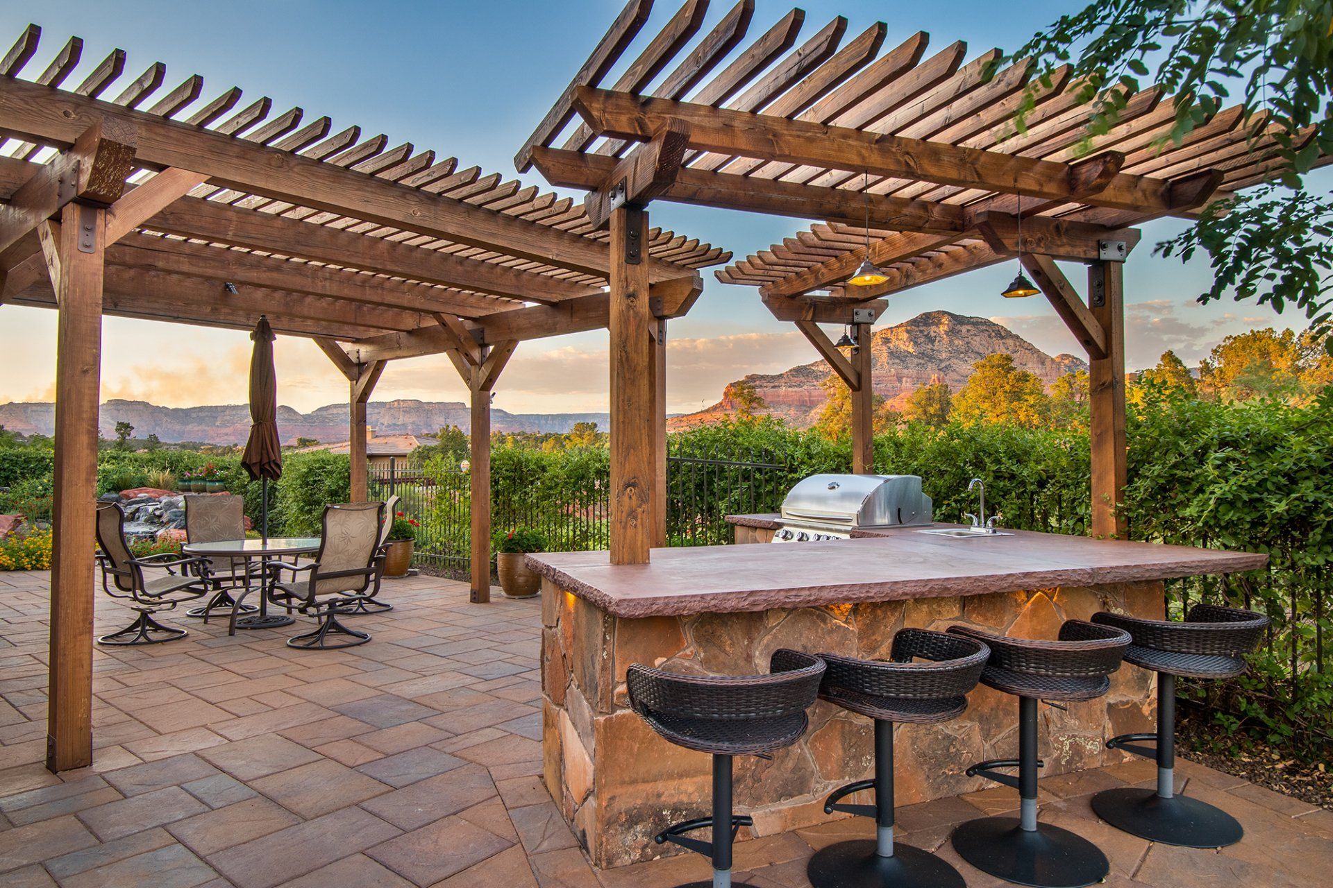 A patio with a pergola , a grill , a table and chairs.