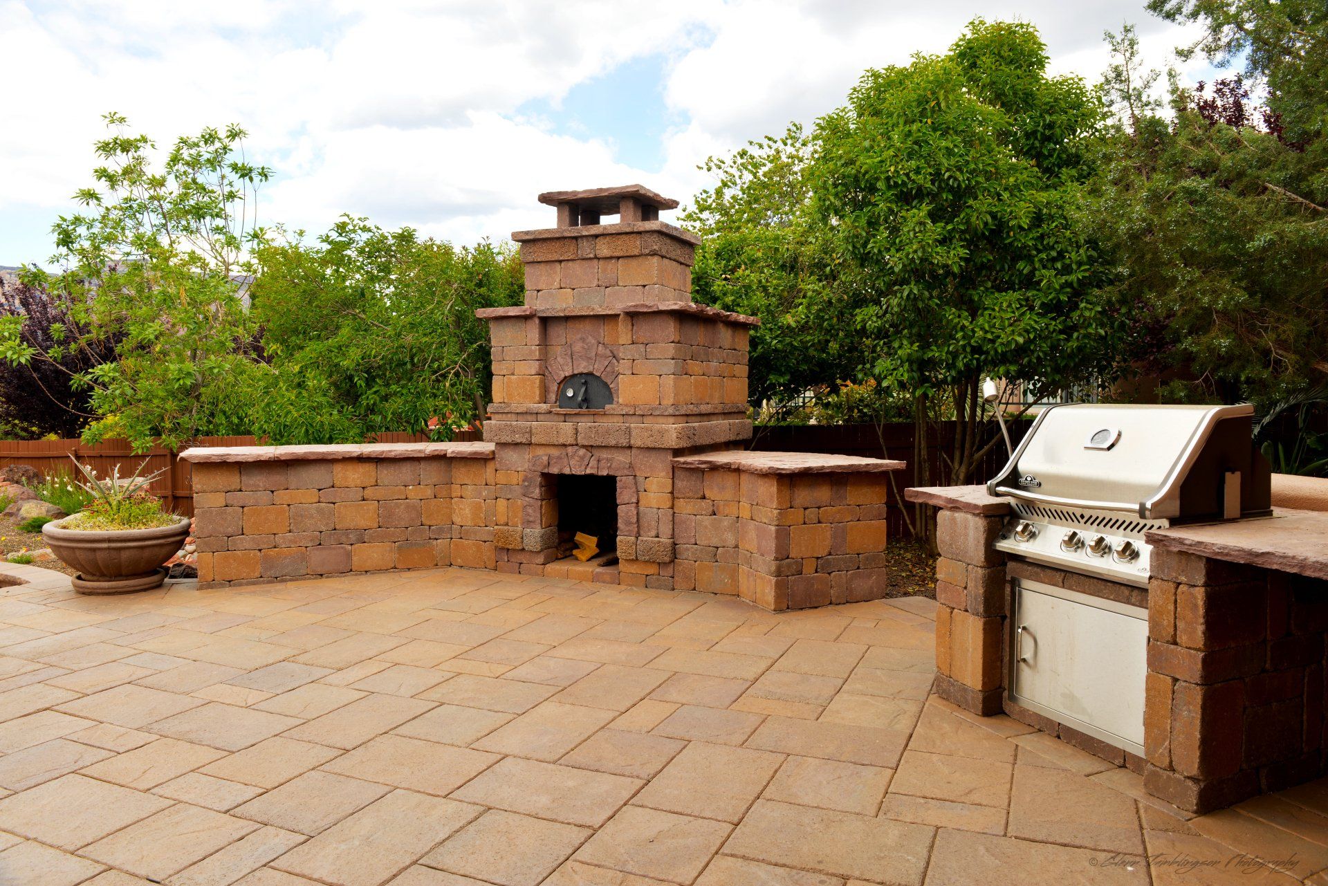 A patio with a grill , pizza oven , and fireplace.