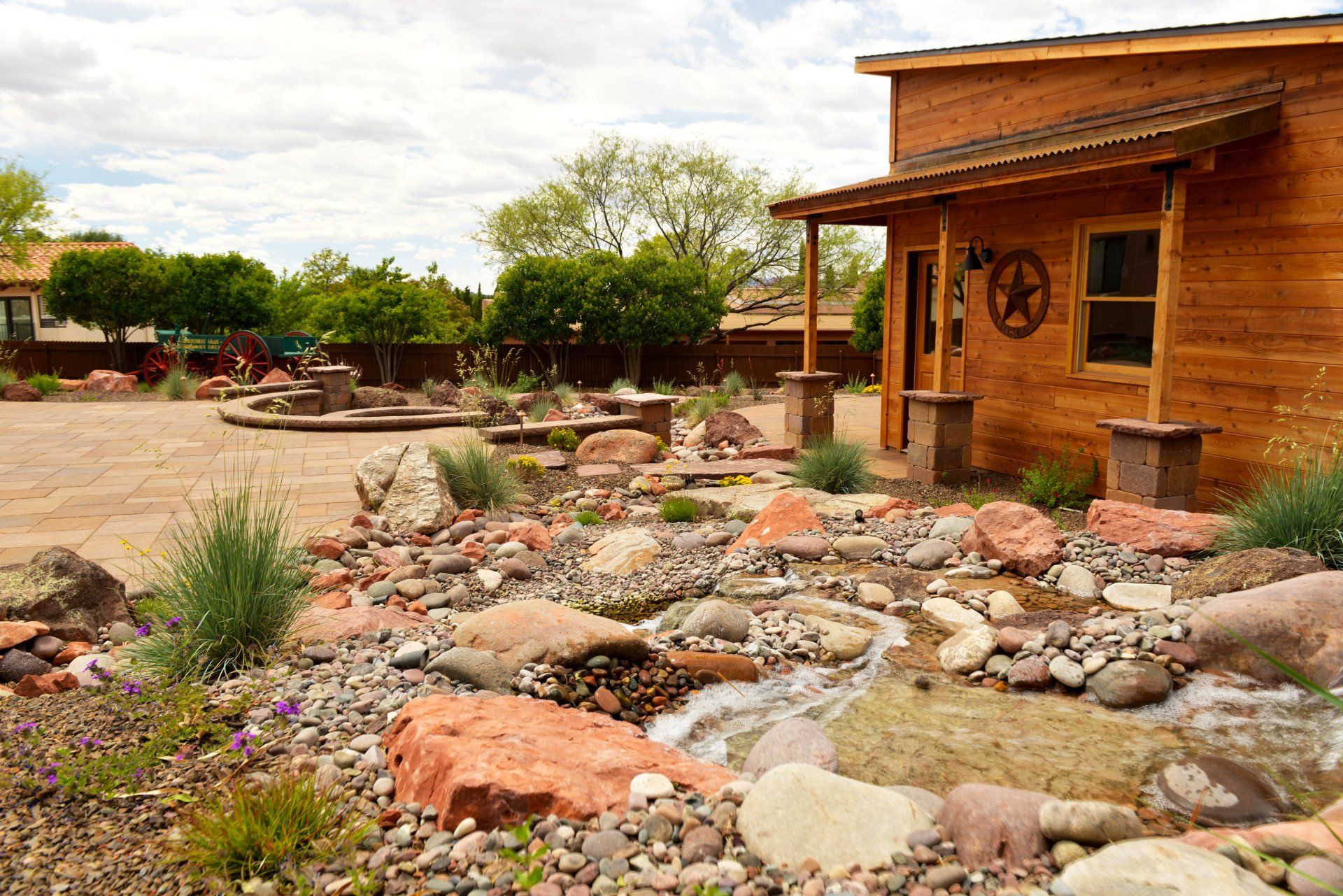 A wooden house with a porch surrounded by rocks and plants.