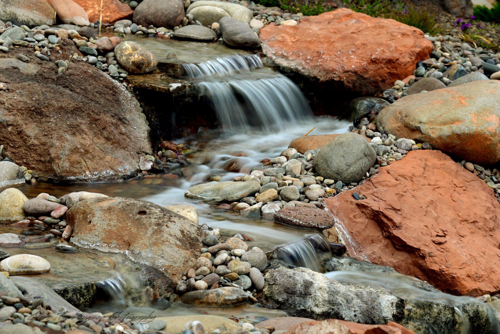 A small waterfall is surrounded by rocks and grass