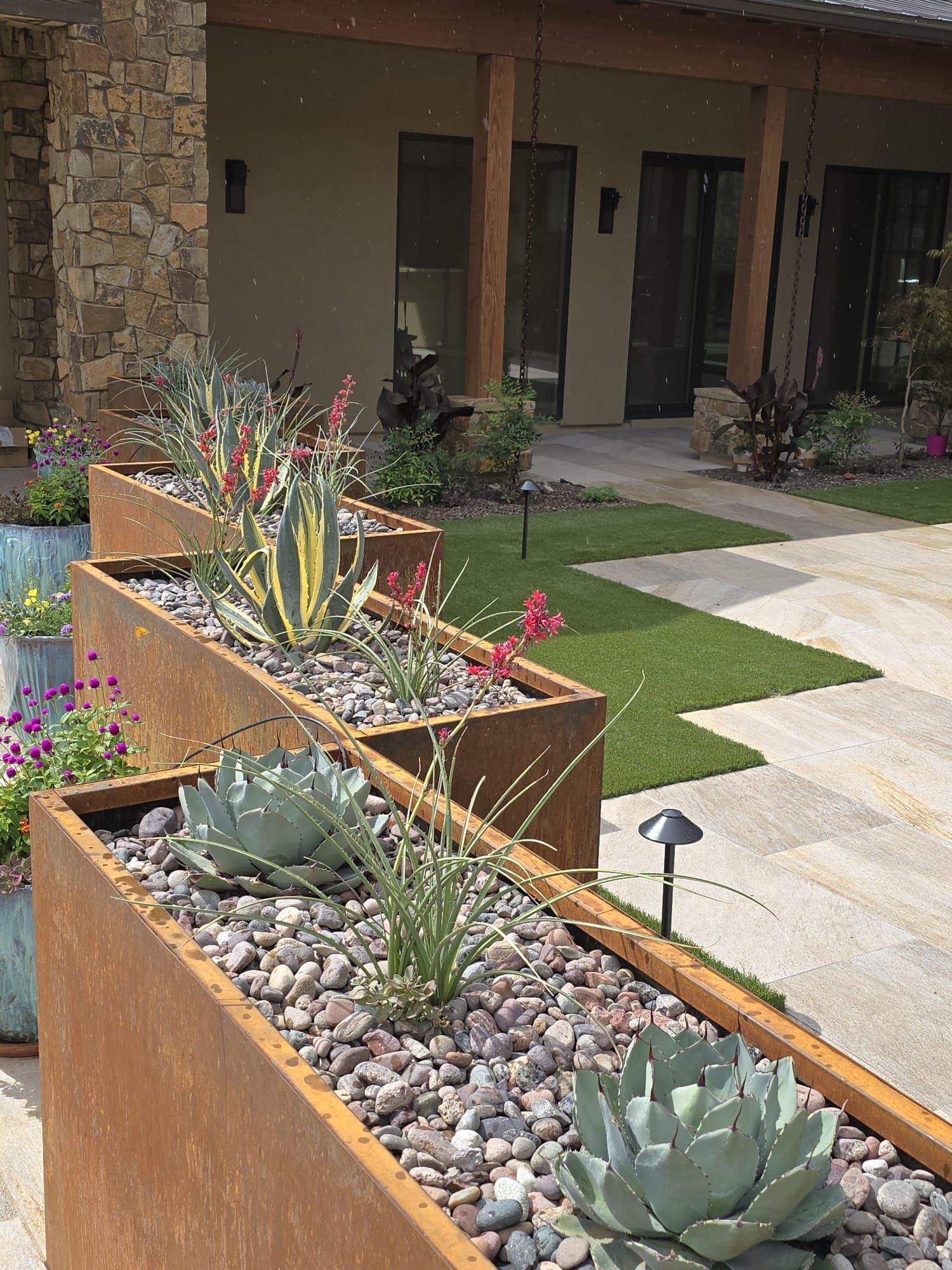 A row of planters filled with plants and rocks in front of a house.