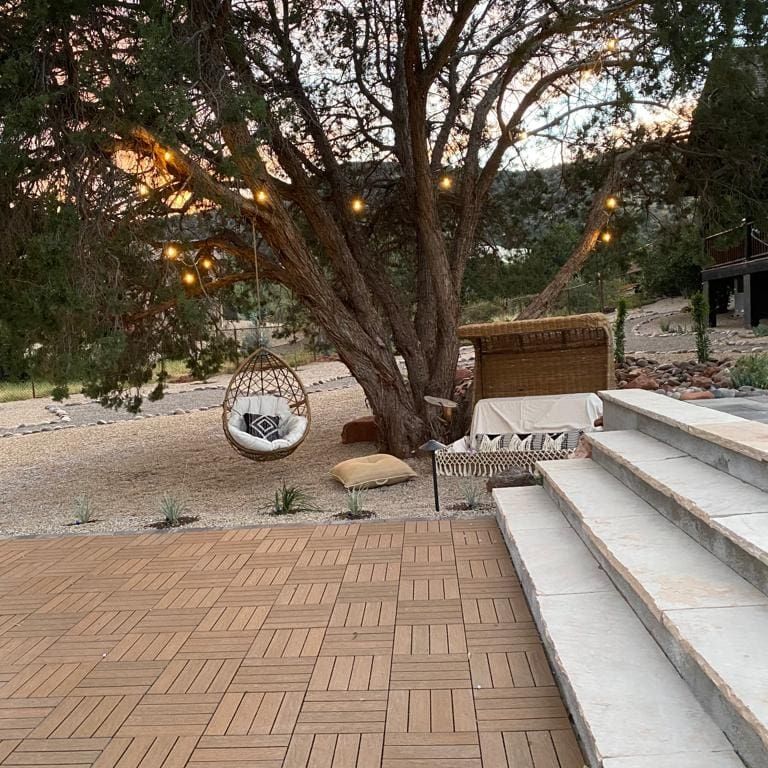 Outdoor patio with a tree, hanging chair, string lights, and stone steps.