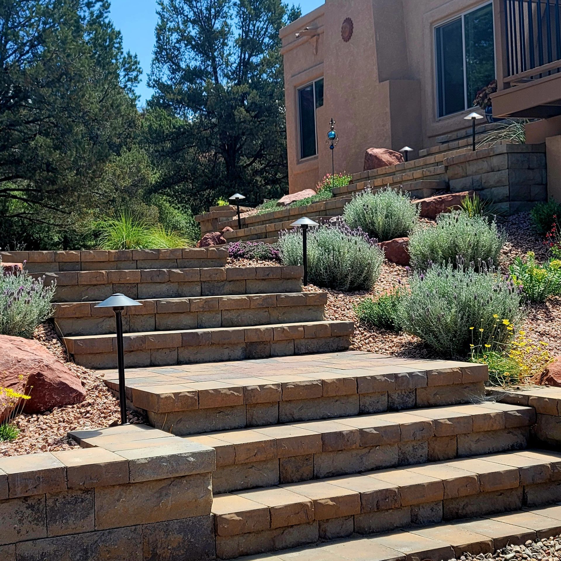 Stone staircase leading up a tiered landscaped yard with shrubs and lights; next to a stucco building.