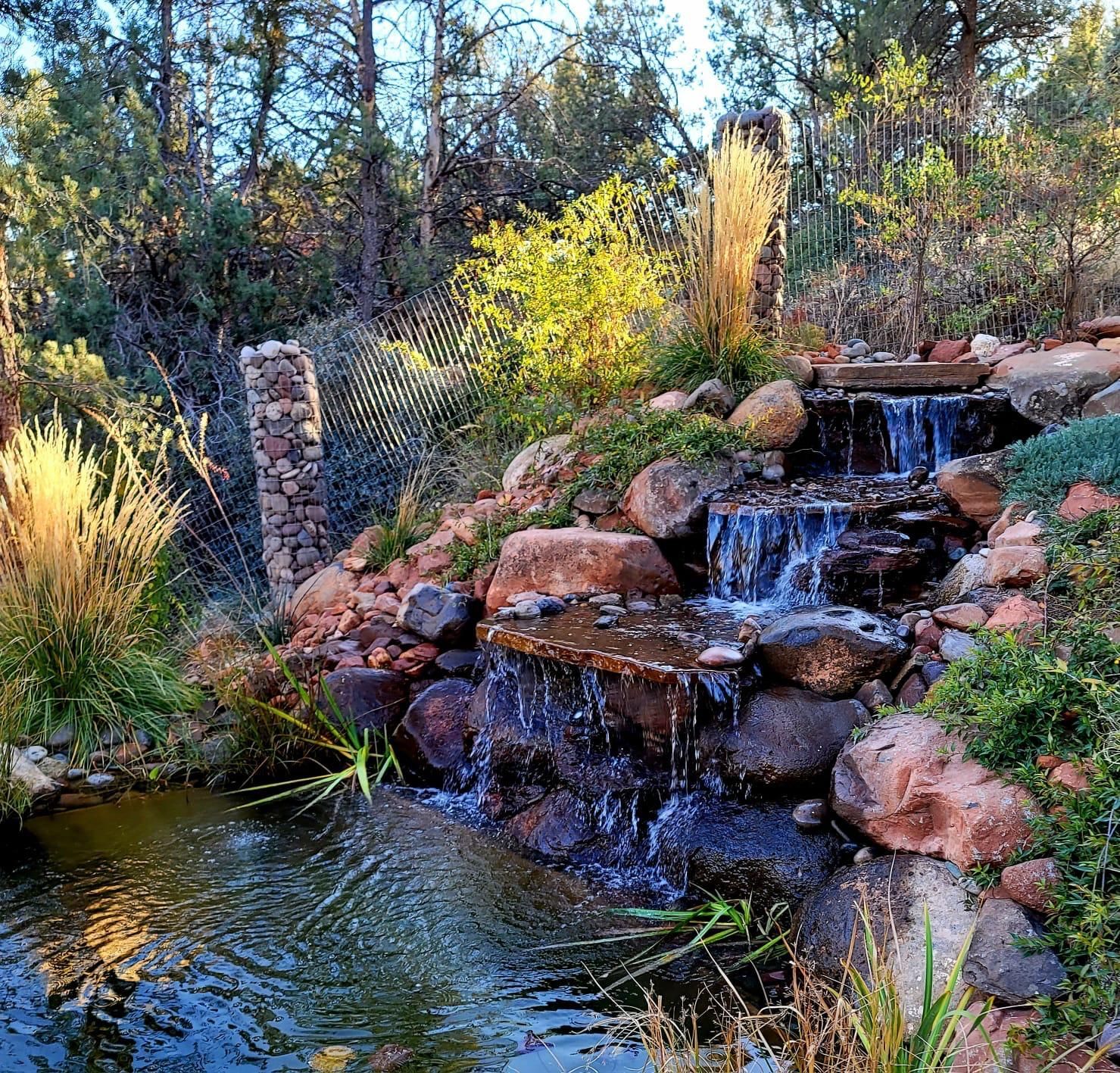 There is a waterfall in the middle of a pond in the woods.