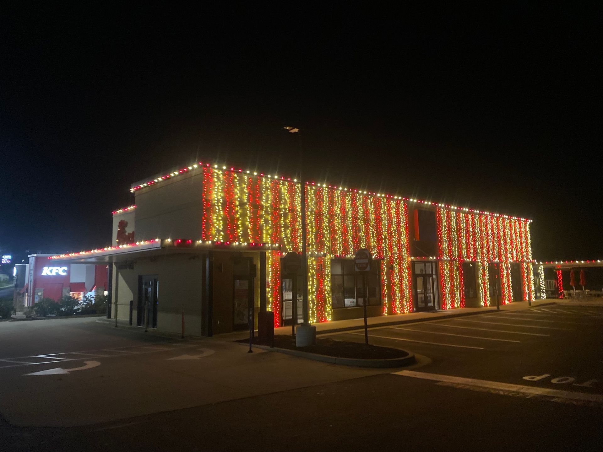 A KFC restaurant at night, decorated with strings of vertical yellow and red holiday lights covering the entire exterior.