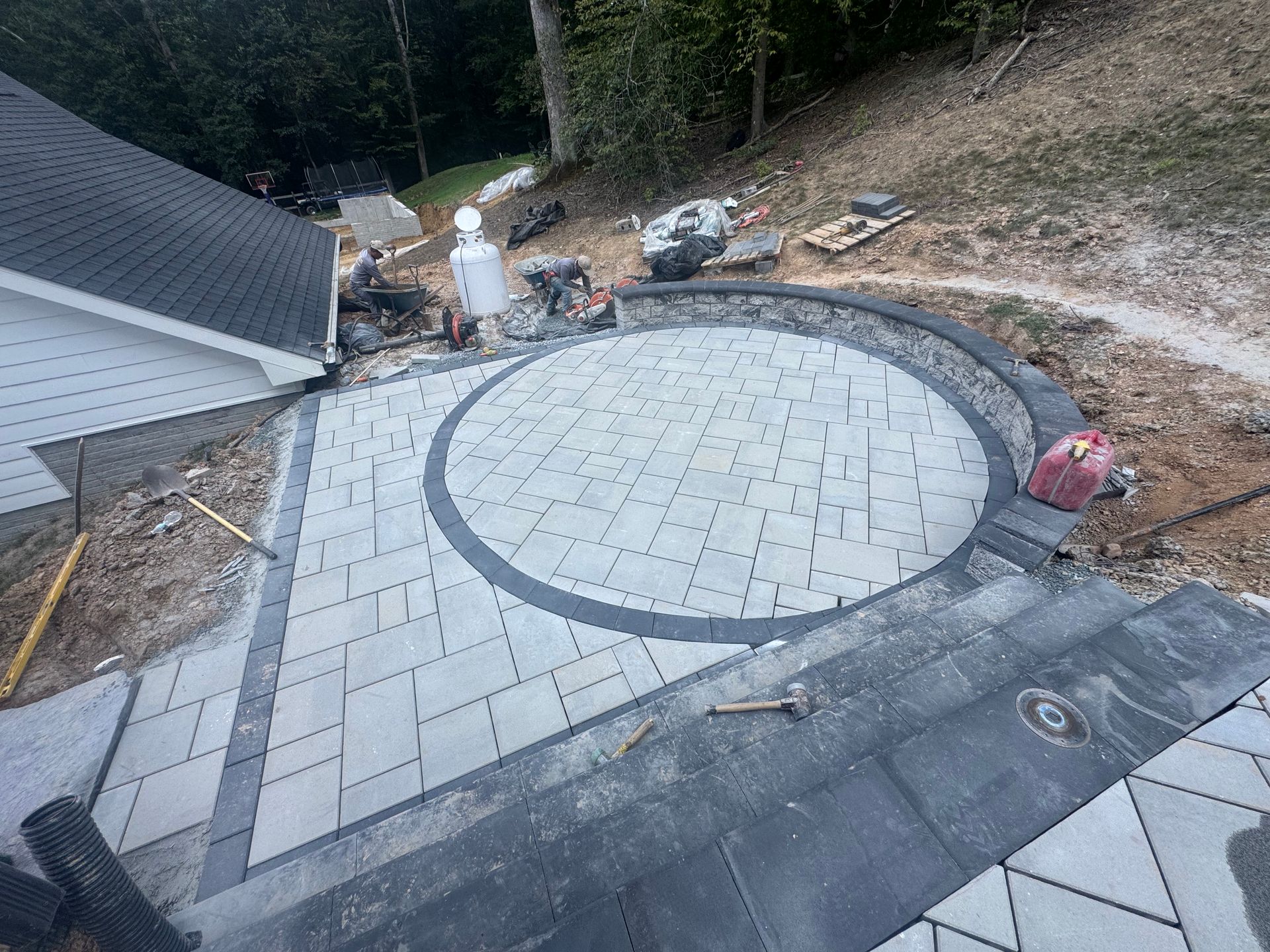 A newly paved backyard stone patio with a circular pattern and stone steps, surrounded by construction materials.
