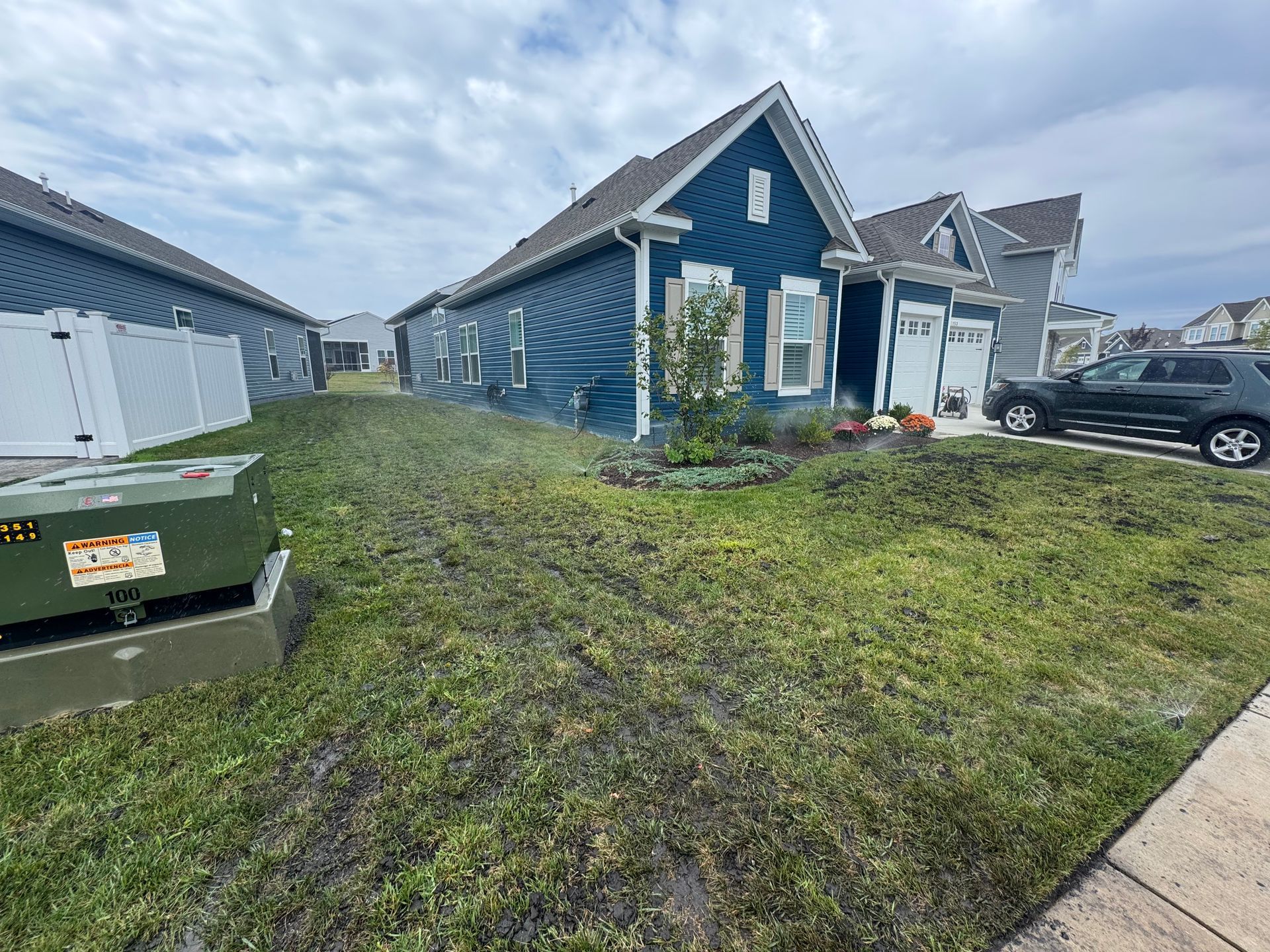 A blue house sits on a suburban lot with a lawn covered in cut grass clippings, with a utility box in the foreground.
