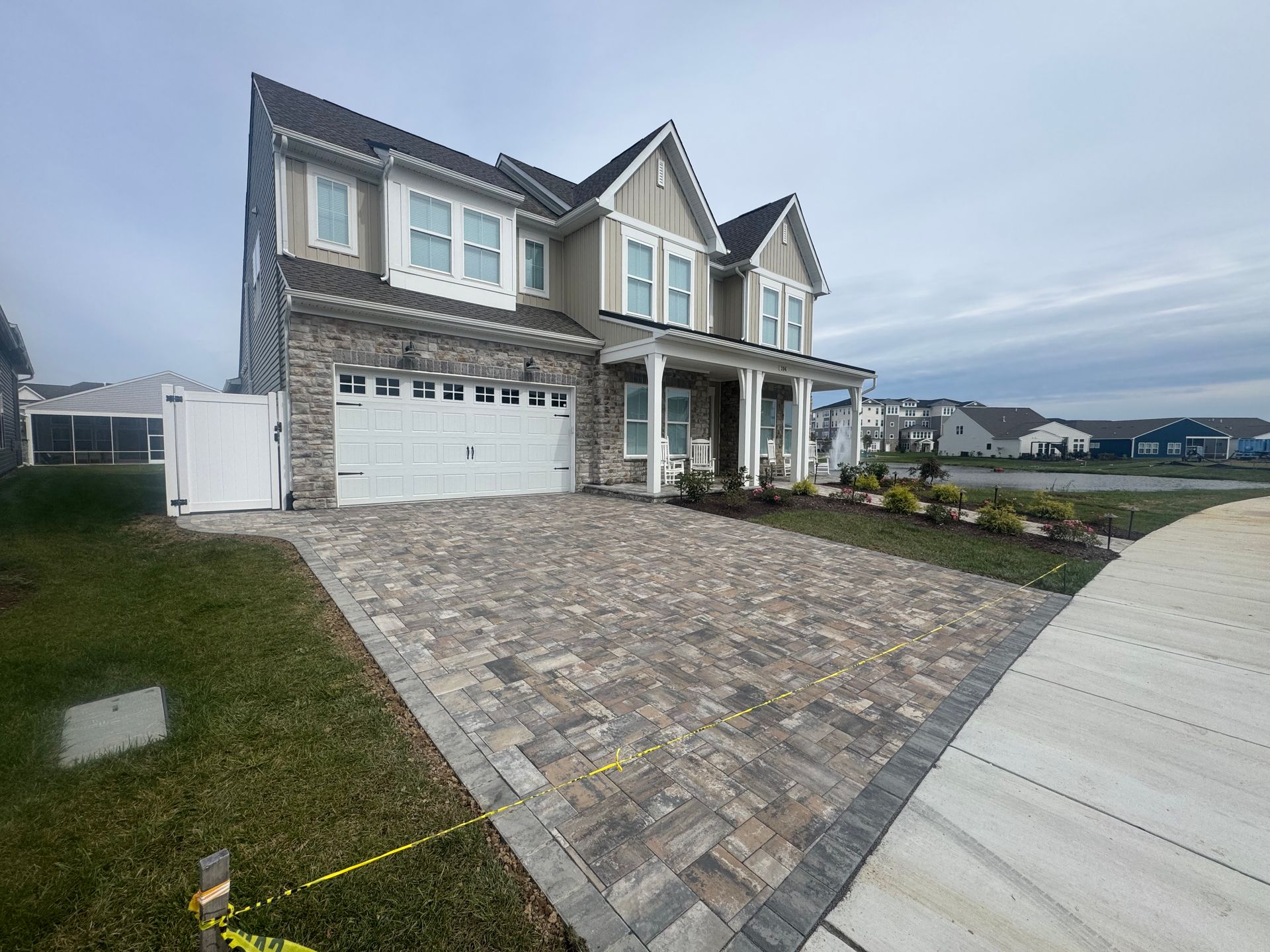 A multi-story house with a stone facade, a white garage, and a newly paved paver driveway under a cloudy sky.
