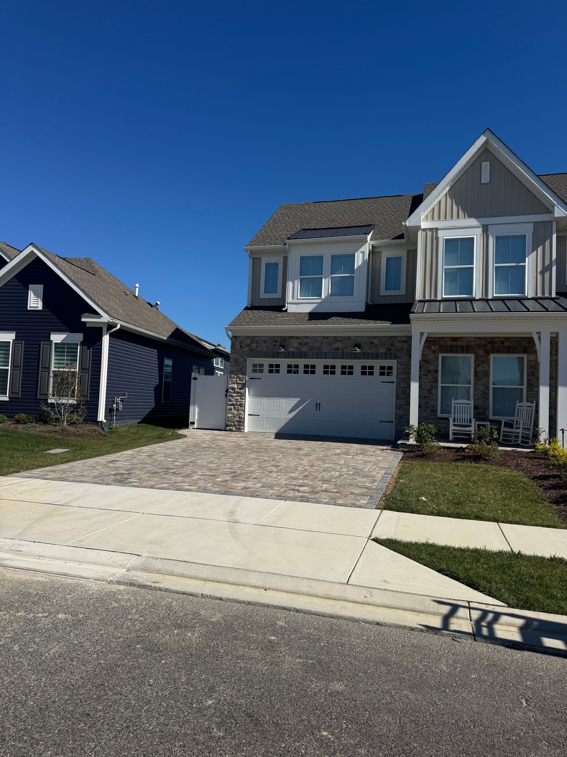 Two suburban houses with a gravel driveway between them under a clear blue sky.