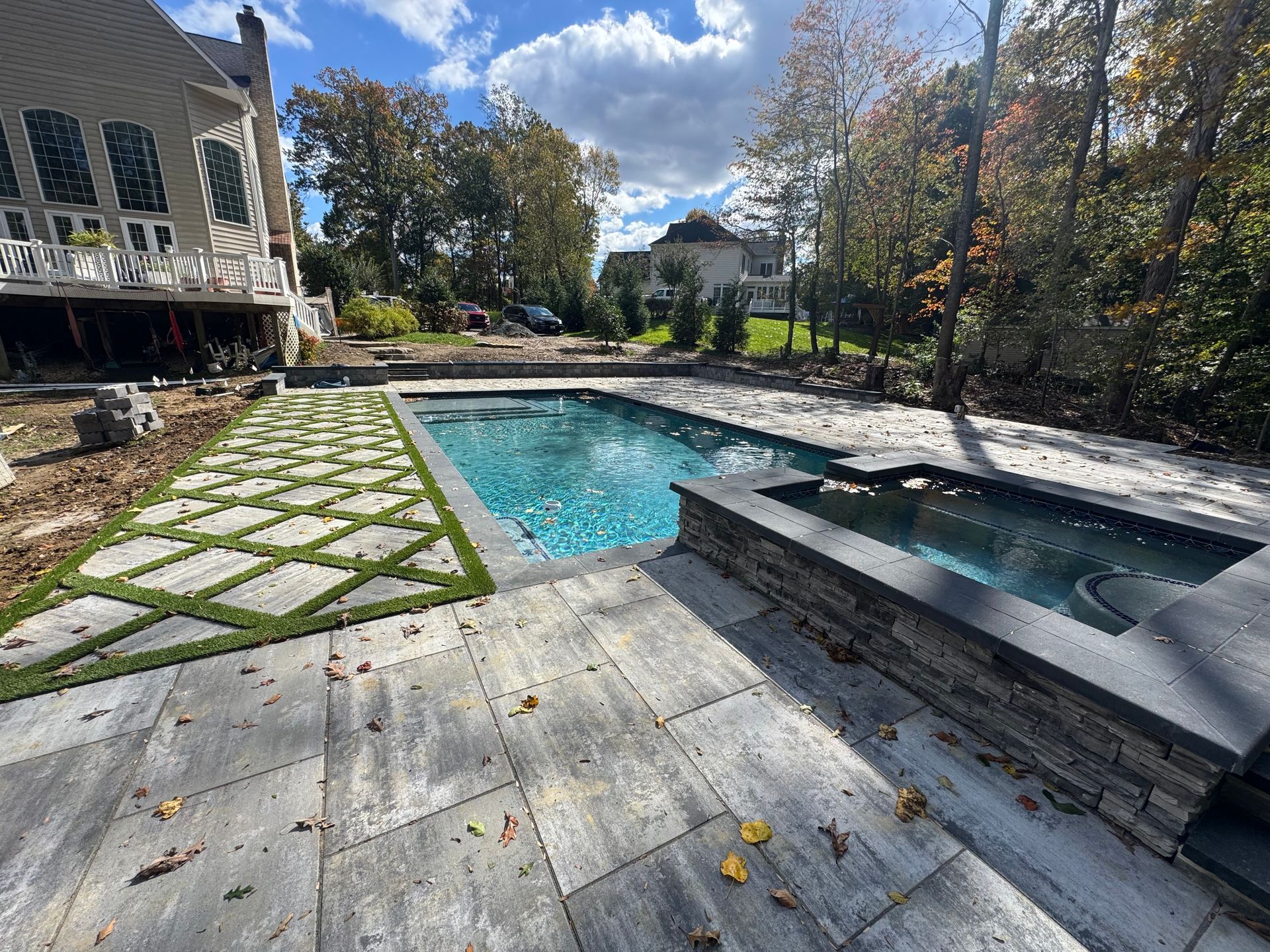 A rectangular pool with an attached spa, surrounded by stone pavers and a geometric diamond-patterned turf pathway.