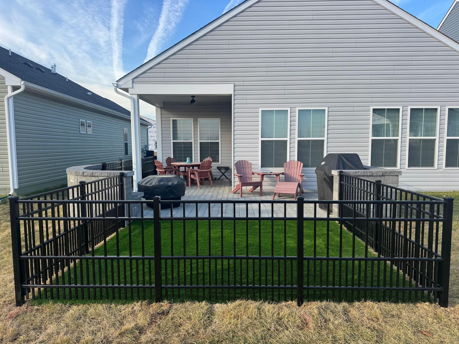 A backyard patio with artificial turf, a black metal fence, and patio furniture under a covered porch.