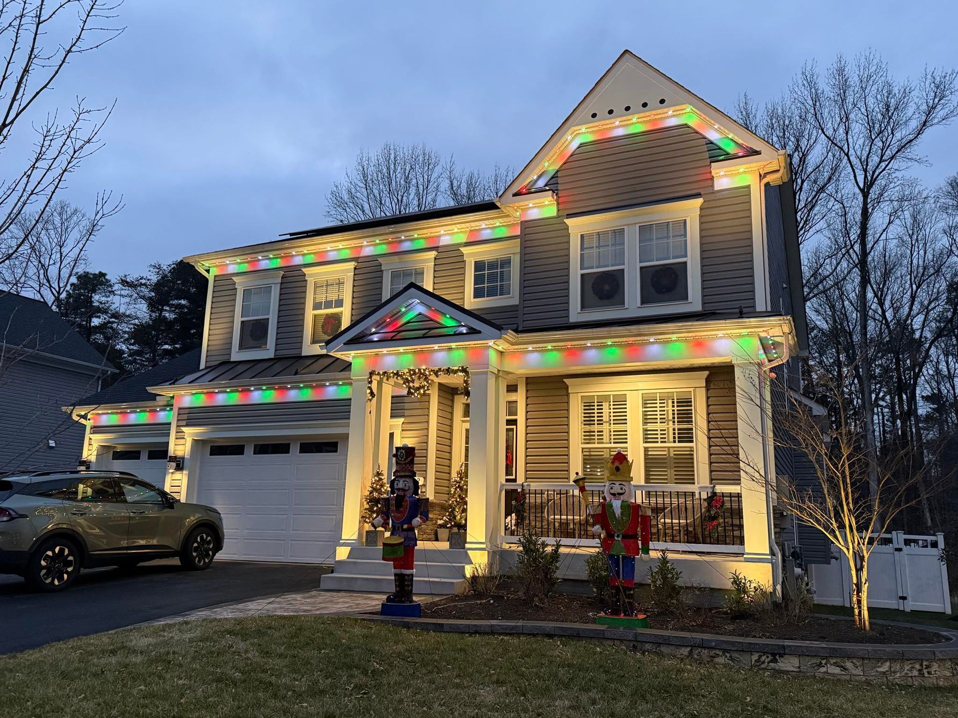 A two-story house at dusk decorated with vibrant, multicolored LED Christmas lights along the rooflines and porch.