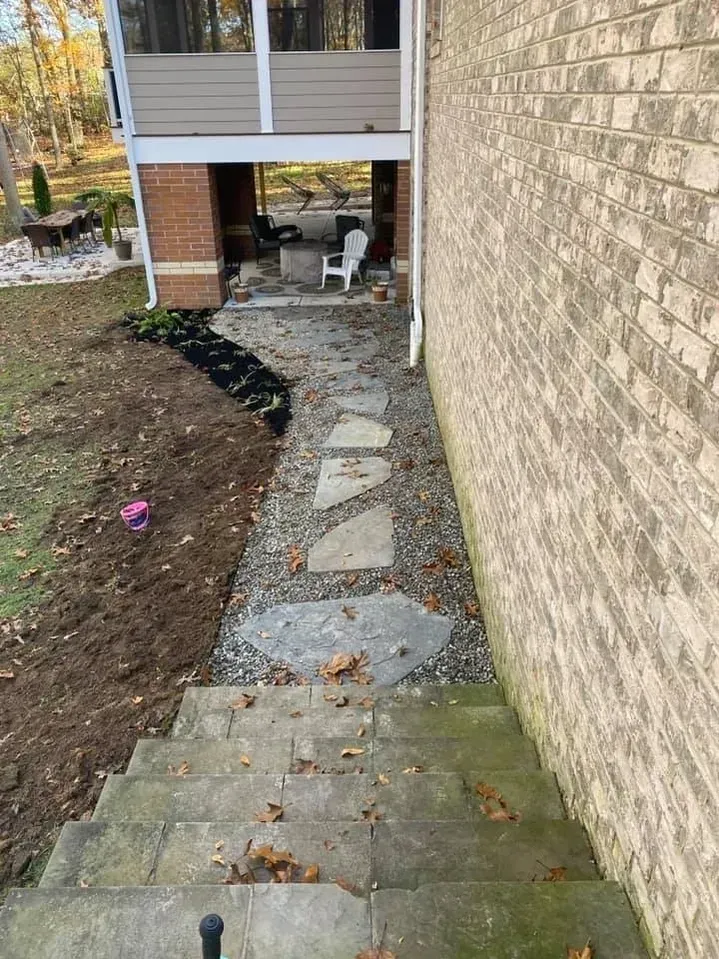 Concrete steps leading down to a flagstone pathway with gravel, beside a tan brick wall and an outdoor living area.
