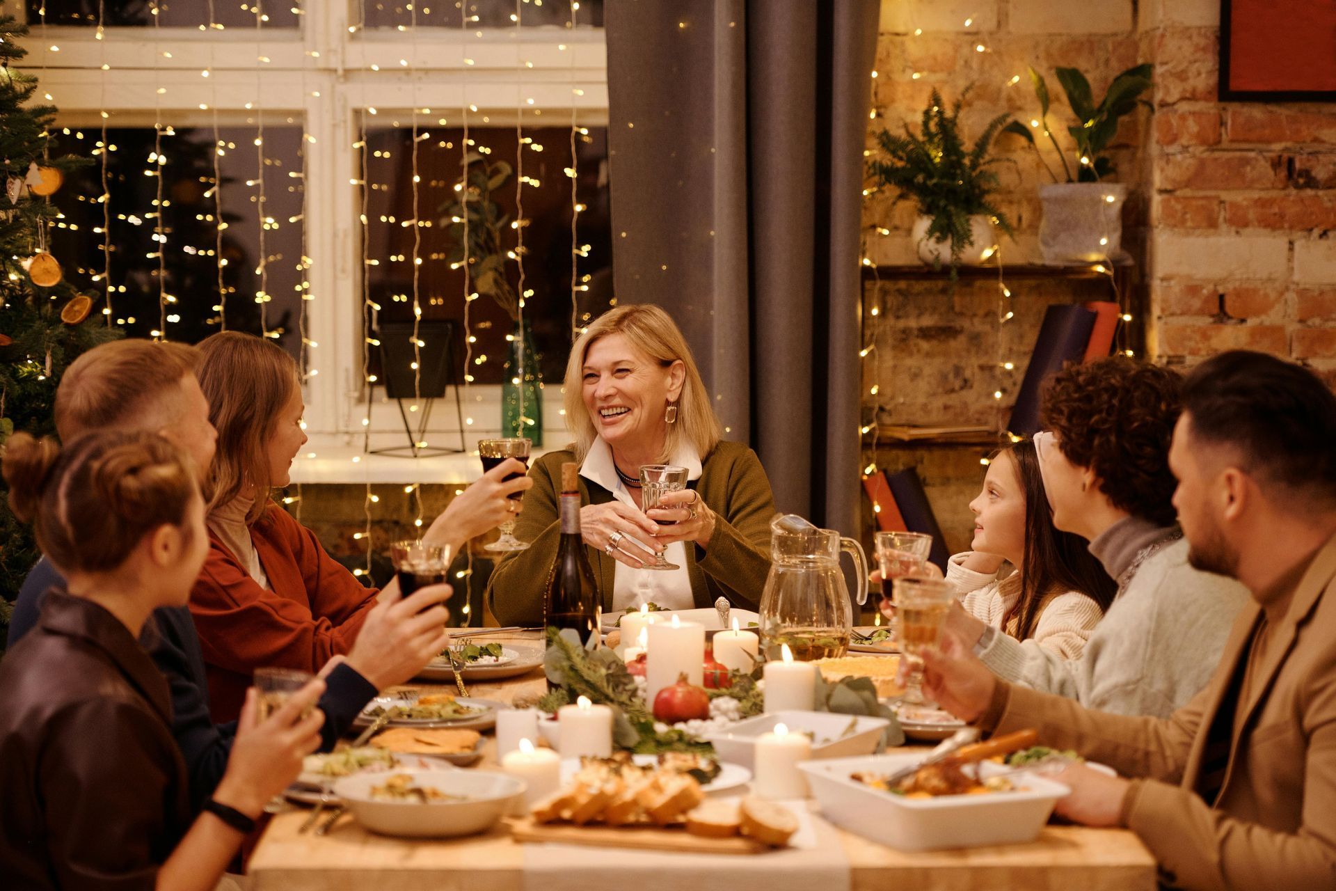 Family enjoying a festive dinner. People gathered around a table, holding drinks, smiling. Warm lighting.