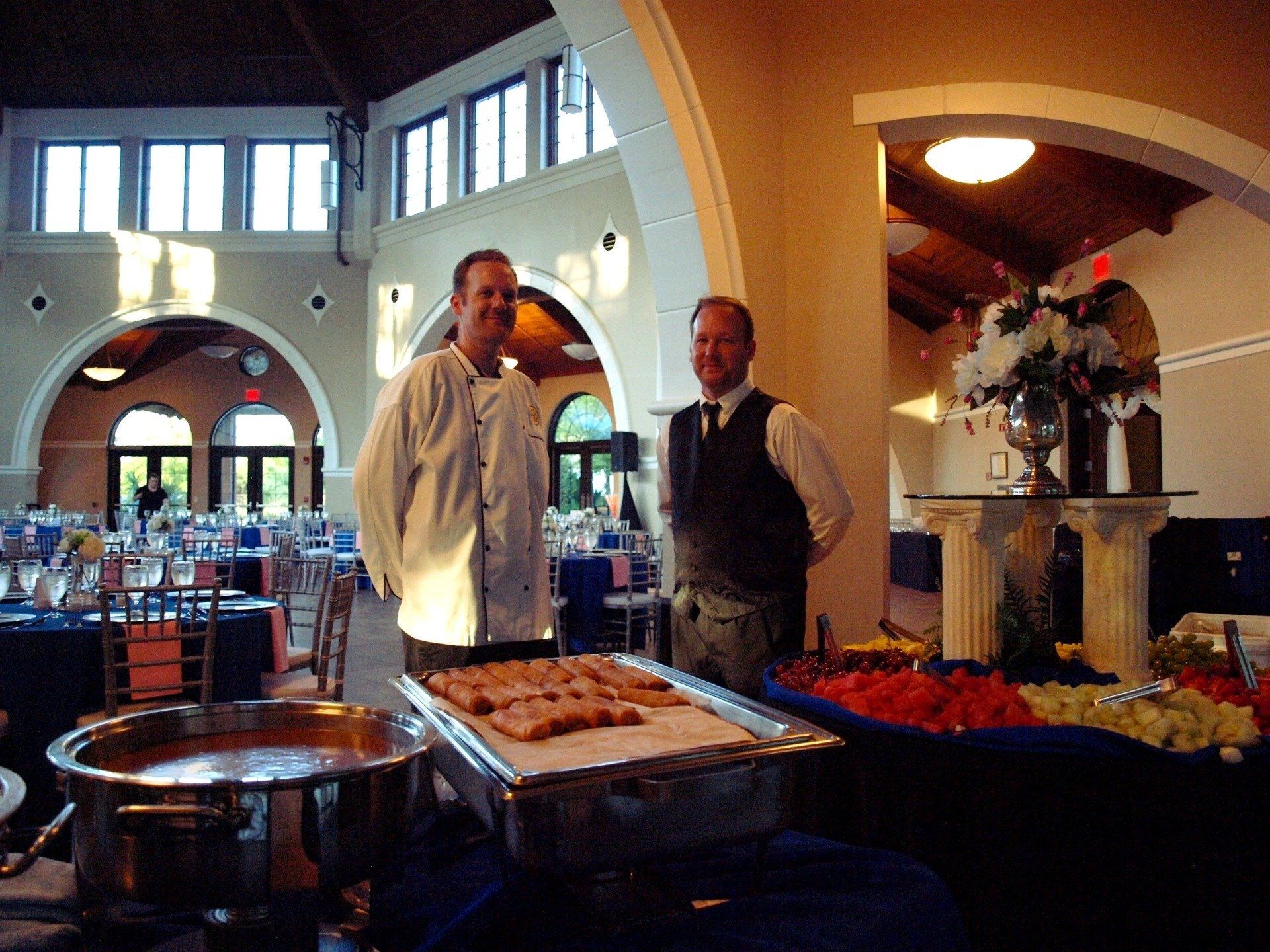 2 male caterers standing behing buffet table