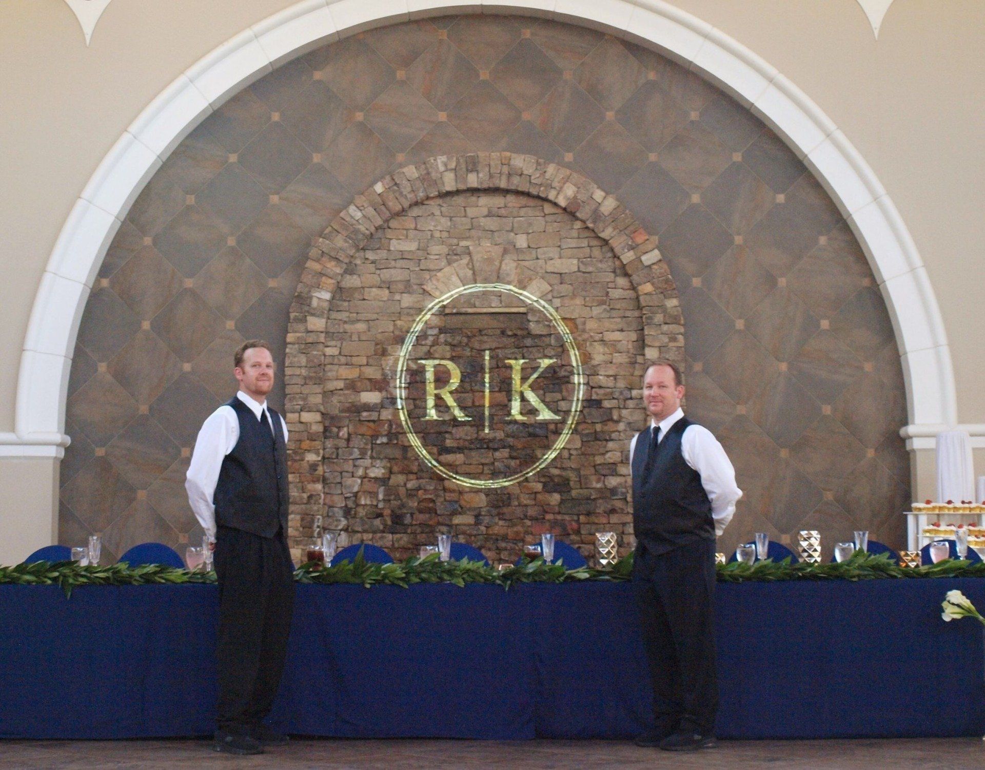 2 male caterers staning in front of wedding party table