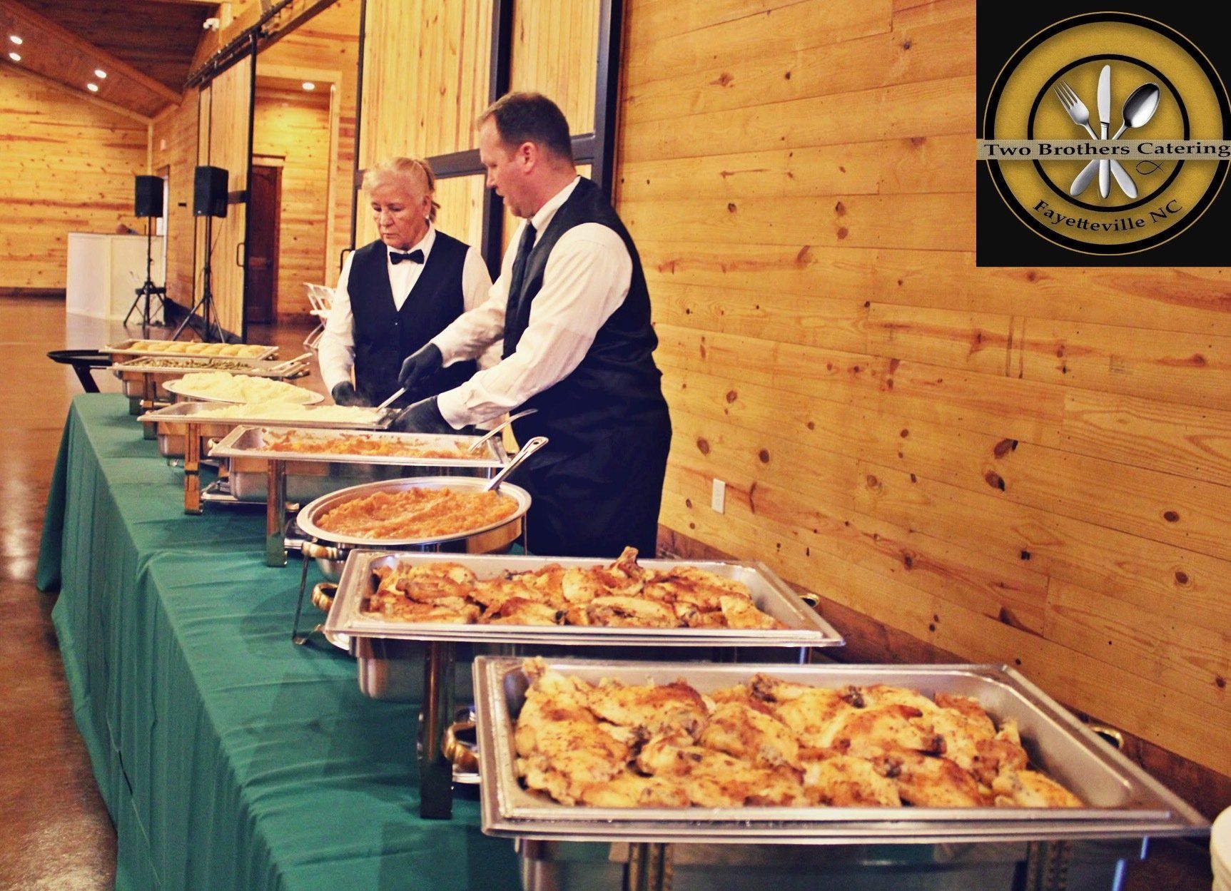 2 caterers setting buffet table with filled buffet pans