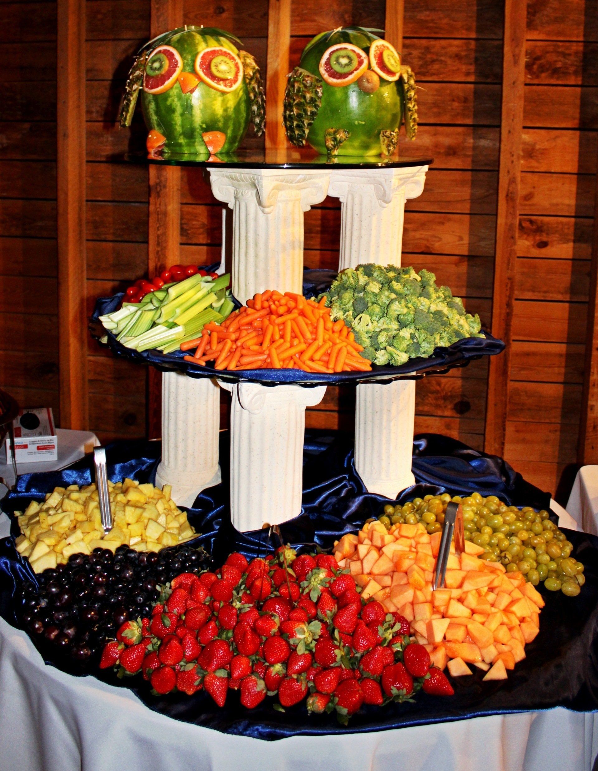 3 tiered fruit and vegetable display with owl statues made of fruit on top