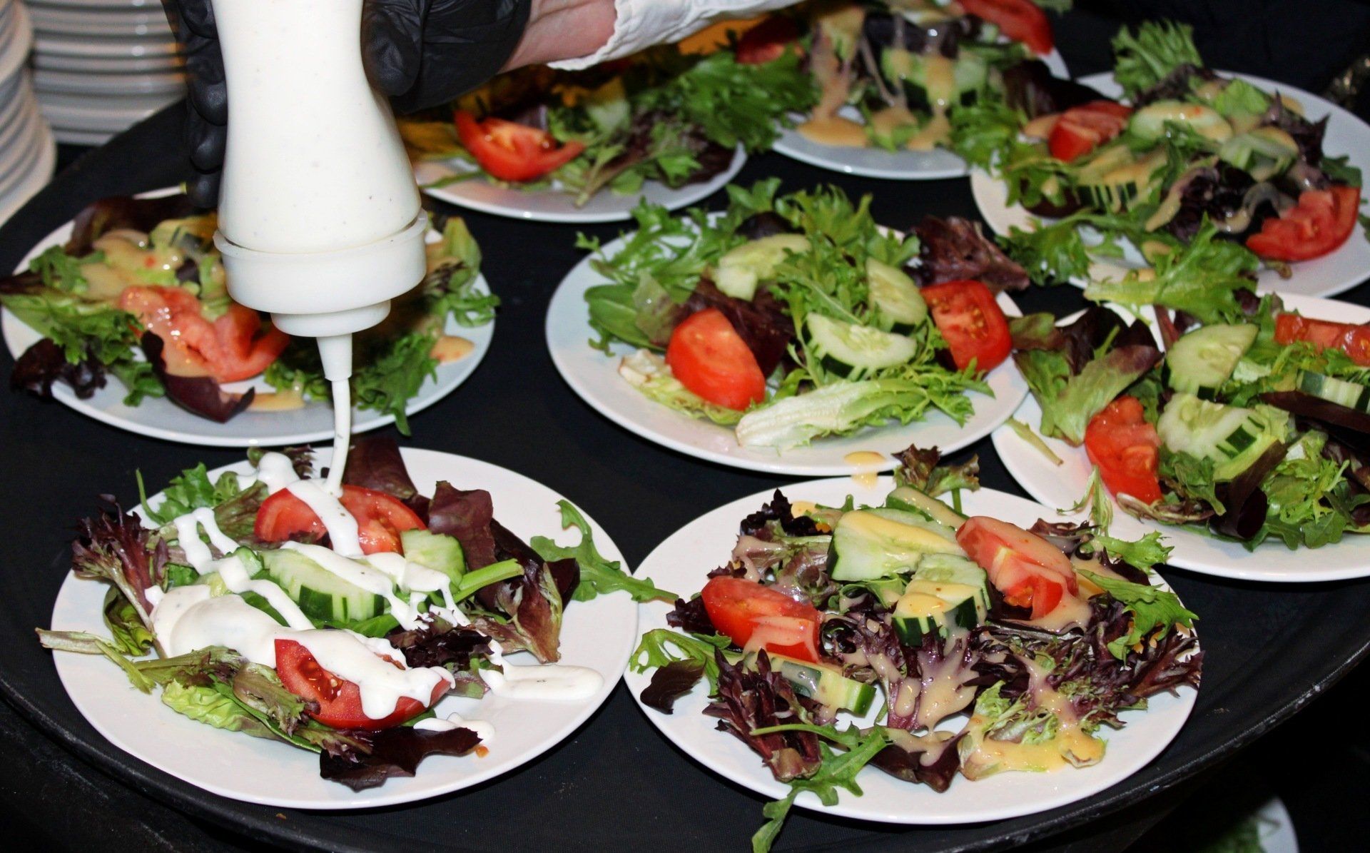 plated salads on tray with salad dressing being added
