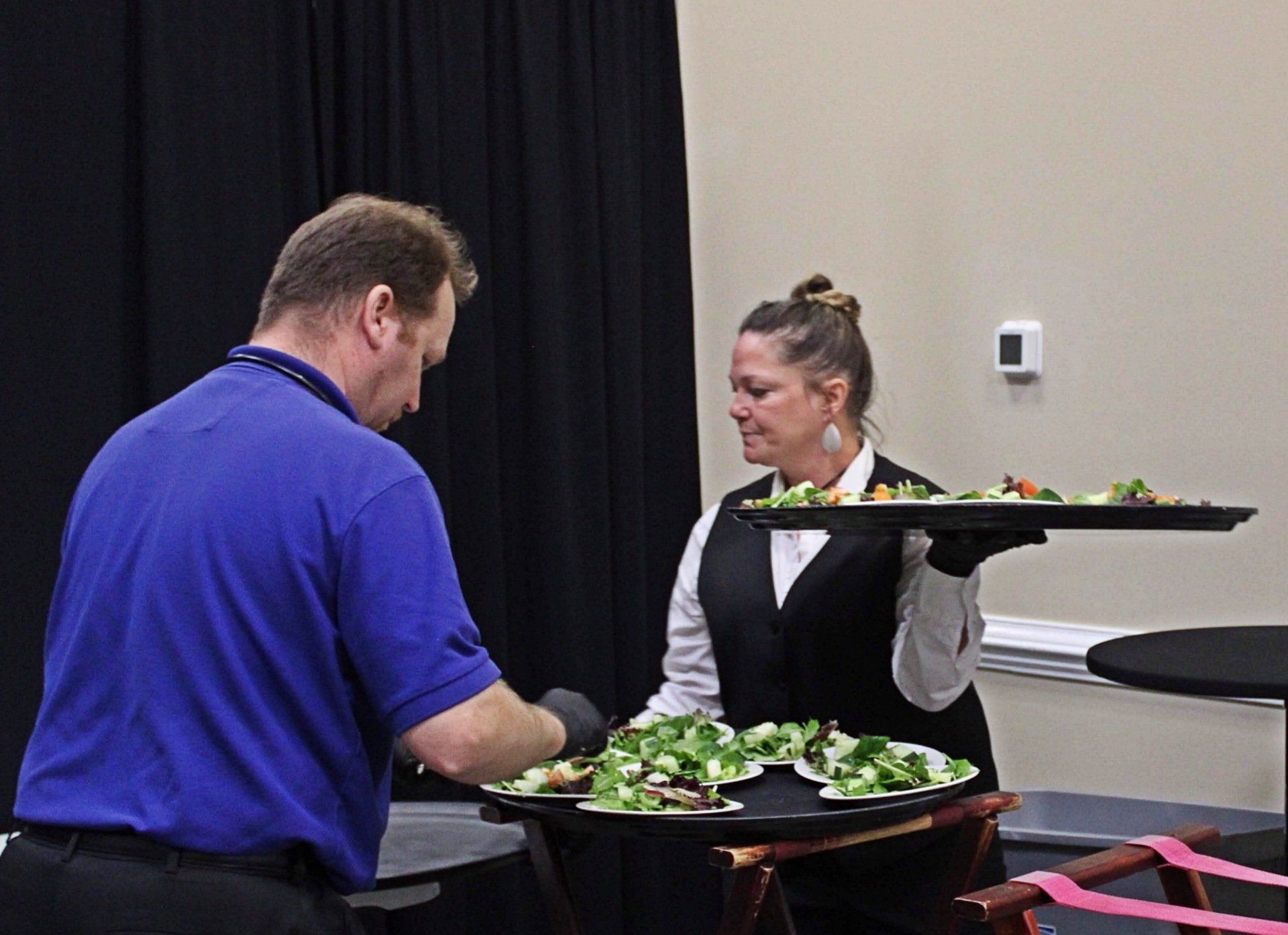 male and female caterer with trays of salads