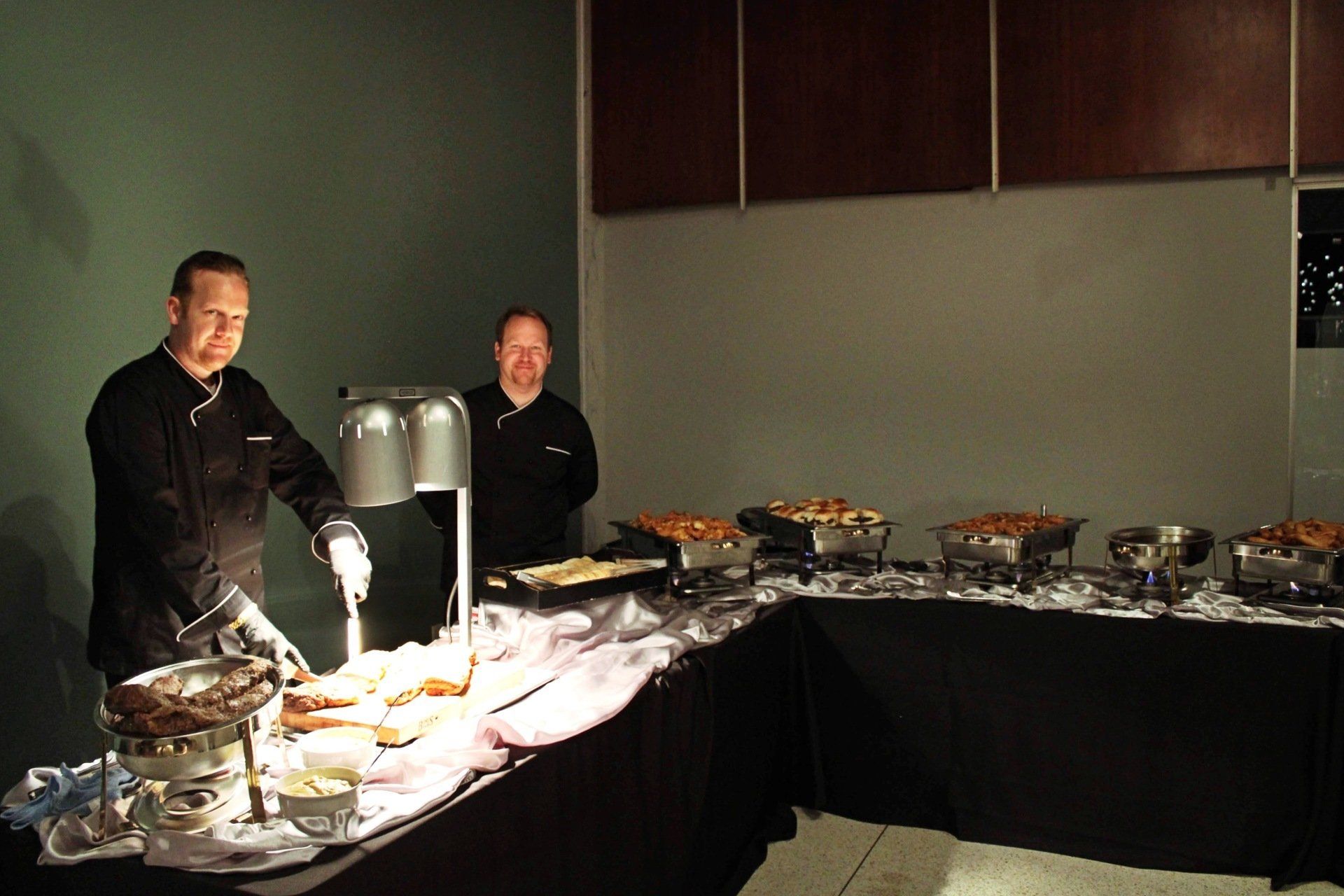 2 male caterers standing behind a carving station and buffet table