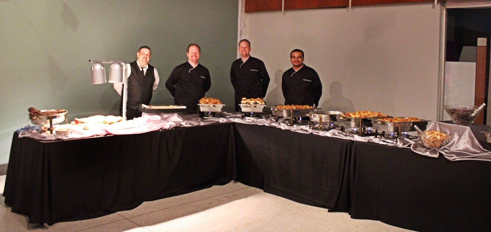 4 male caterers standing behind a carving station and buffet table