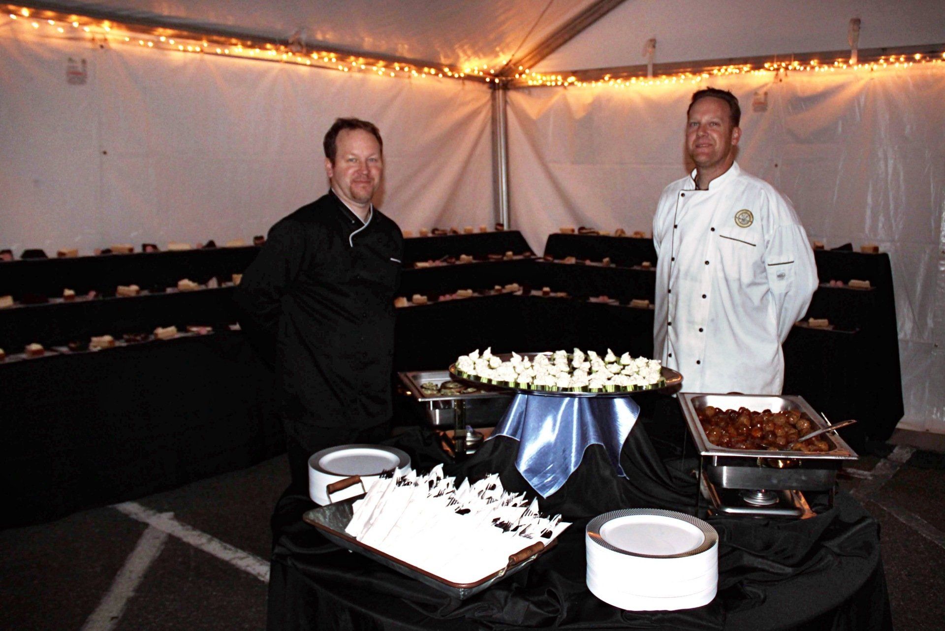 2 male caterers standing behind a round appetizer table