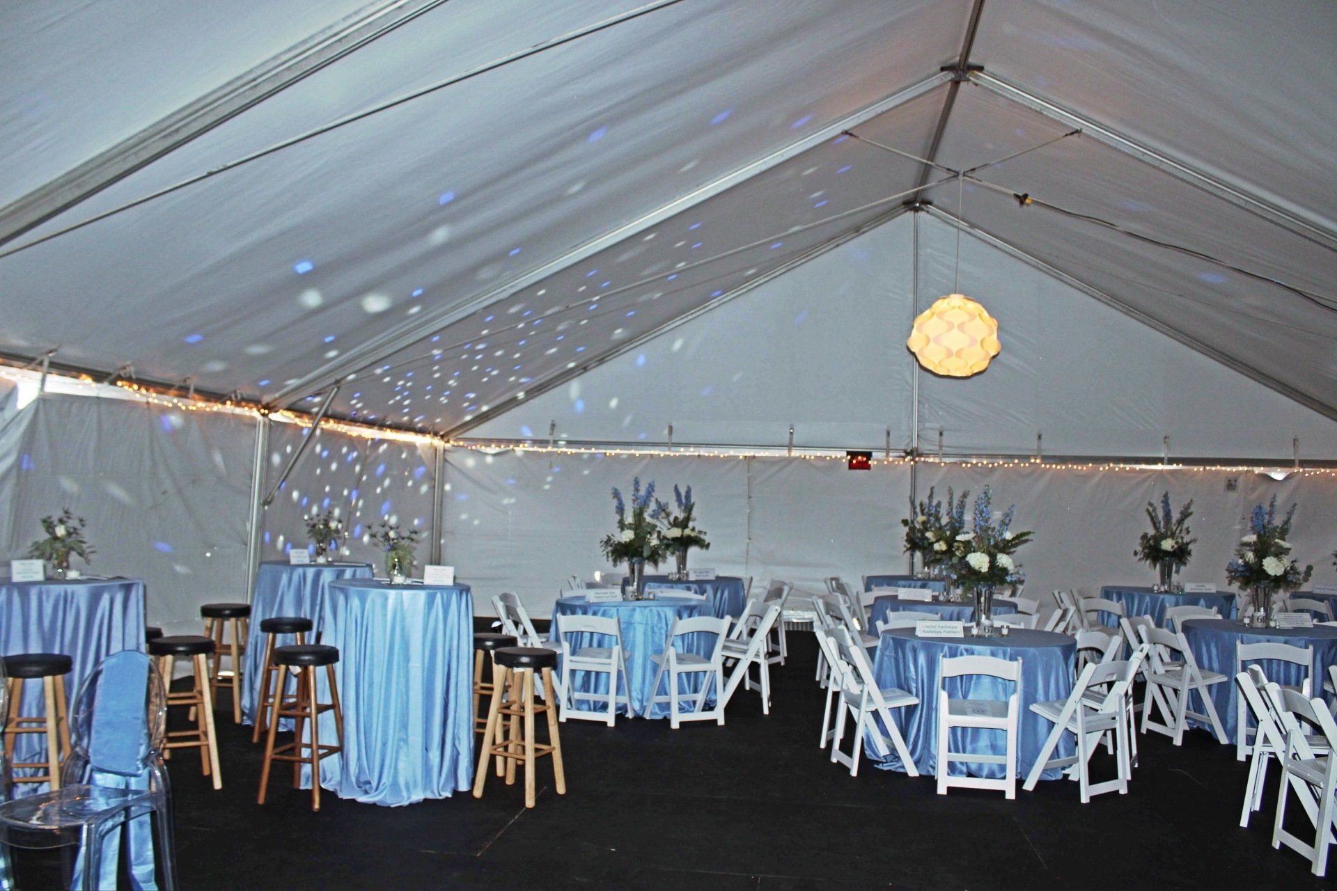 tented room set with round tables in a blue and white decor with floral centerpieces