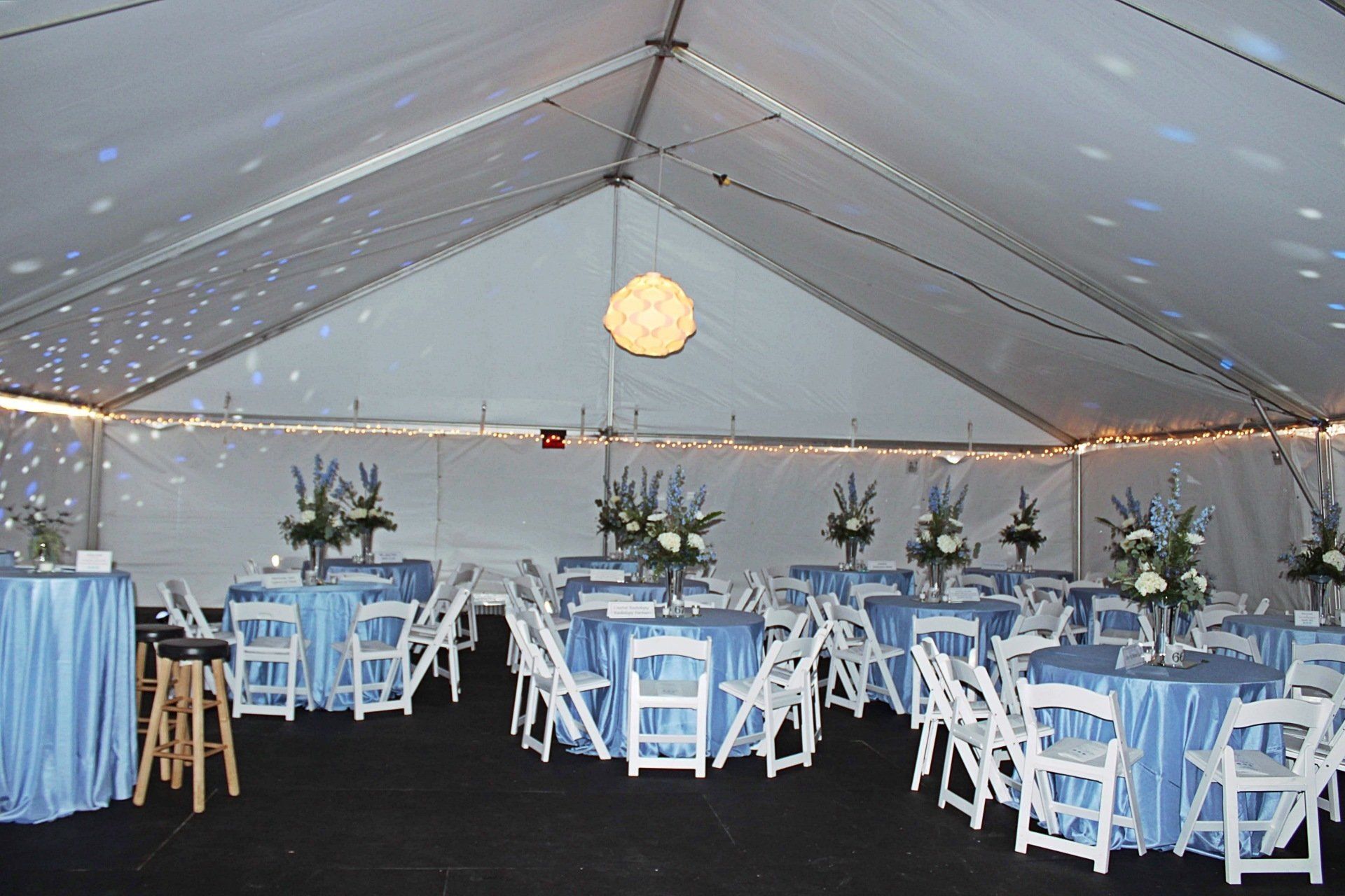 tented room set up with round tables in a blue and white decor and floral centerpieces