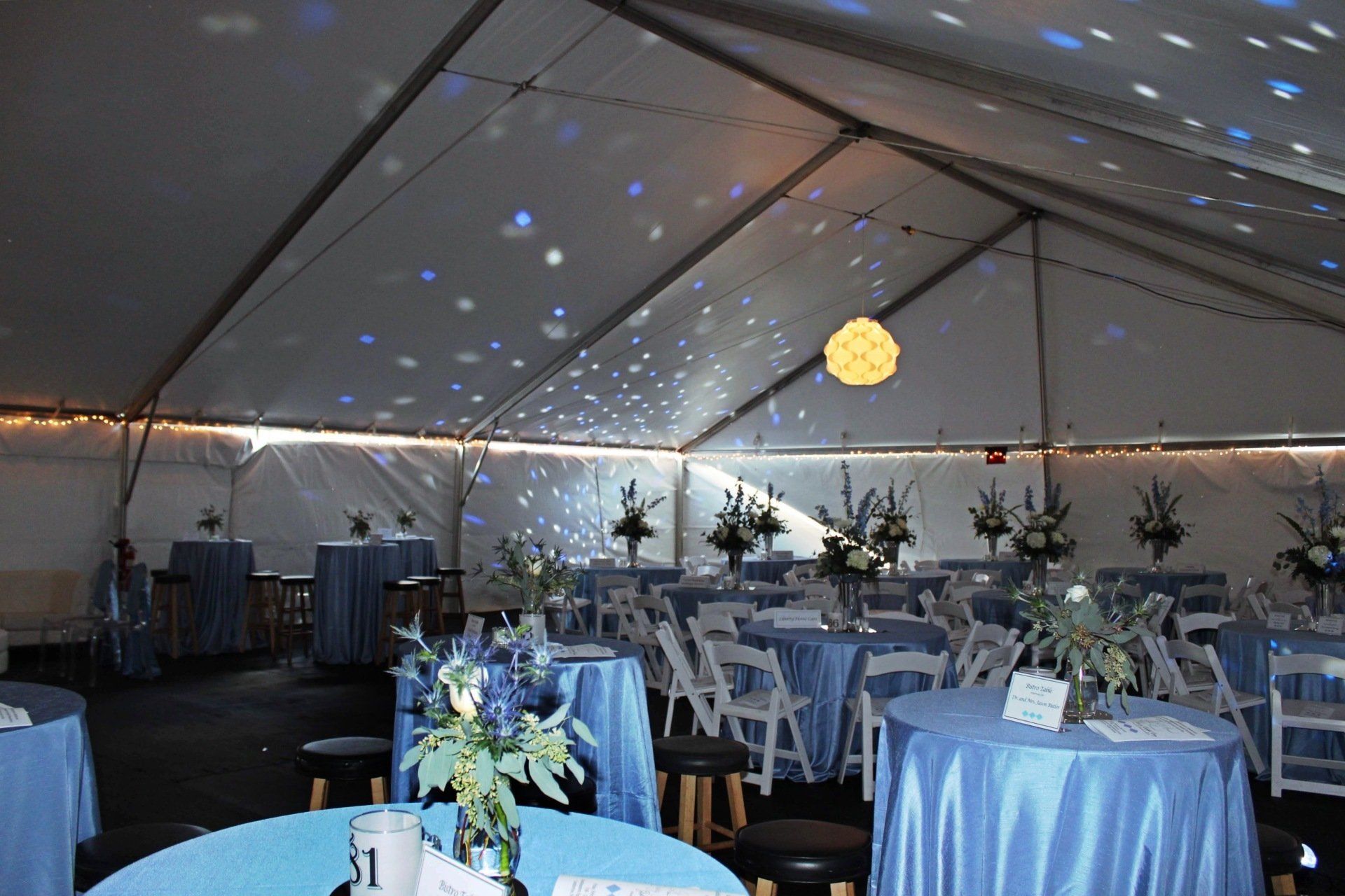 tented room set up with round tables in blue and white decor and floral centerpieces