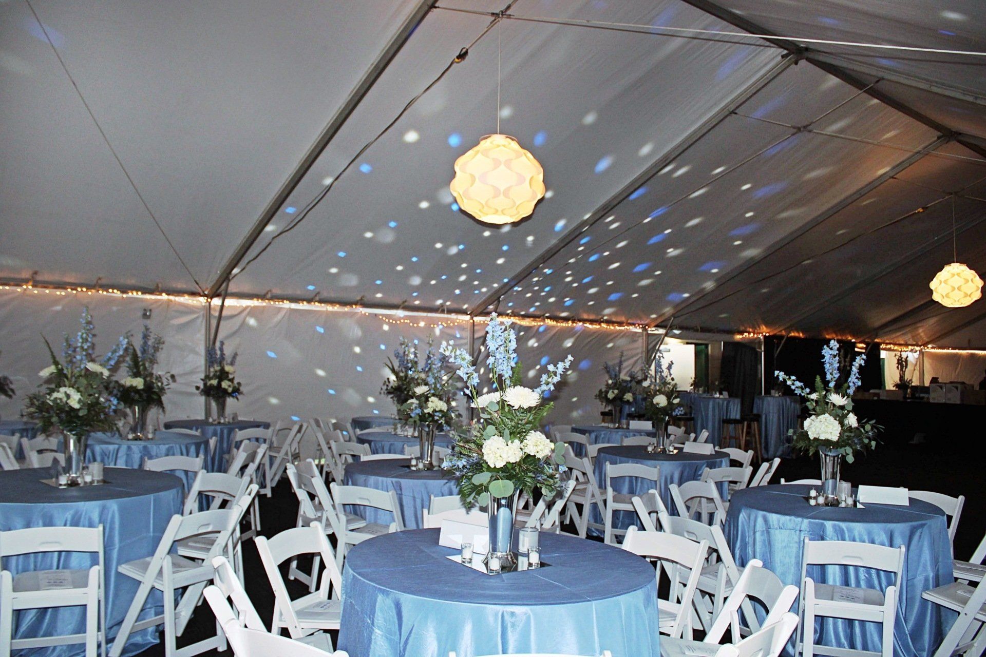 tented room set up with round tables in blue and white decor with floral centerpieces