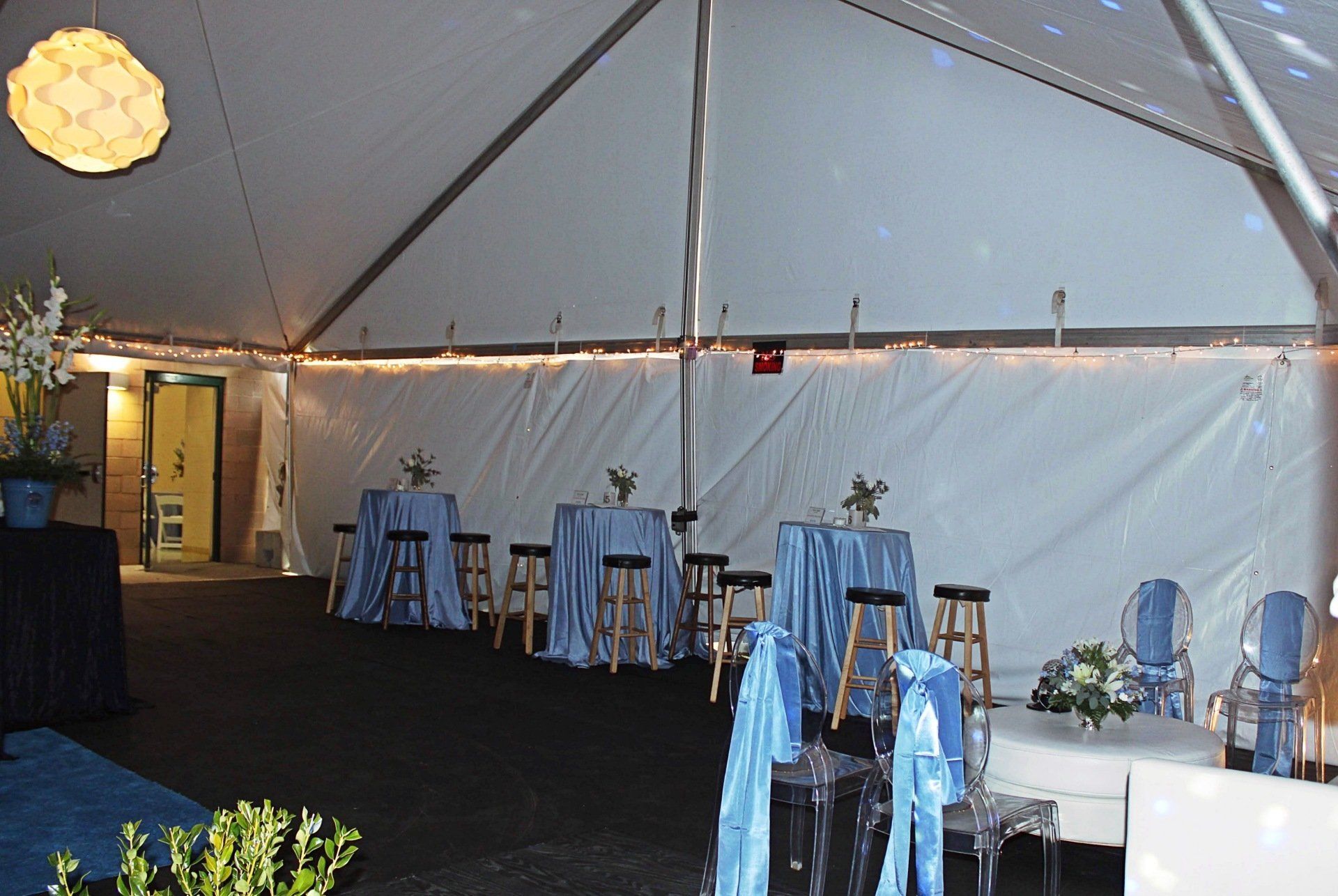 tented room with round hightop tables in blue and white decor with floral centerpieces