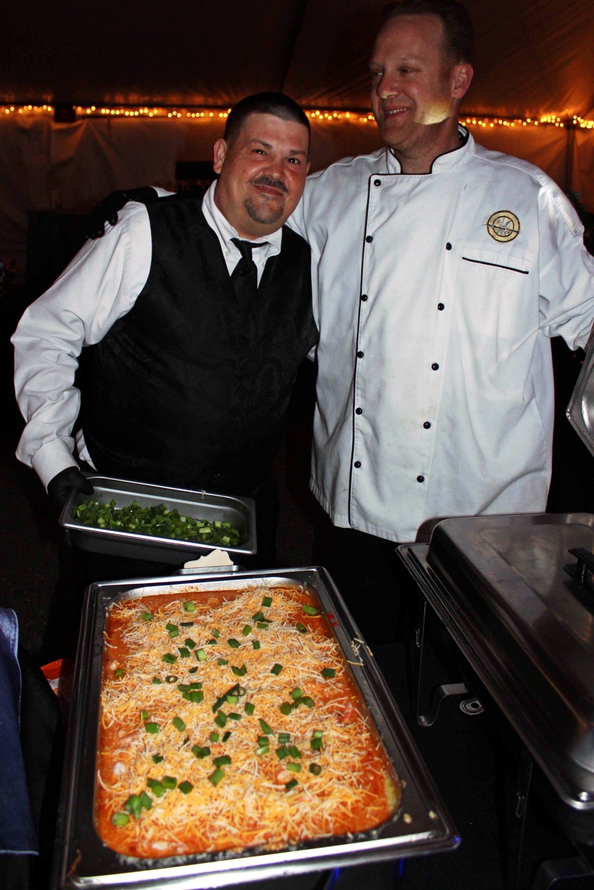 2 male caterers standing behind a full buffet pan