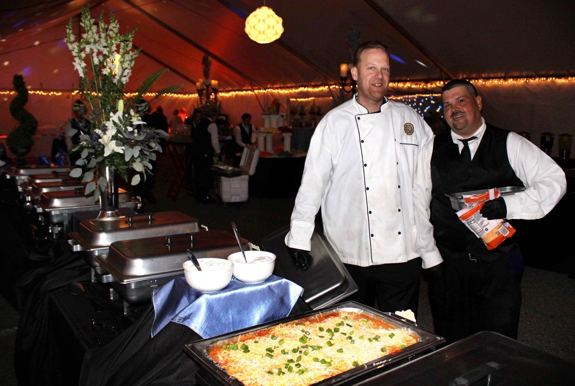 2 male caterers standing behind a buffet table