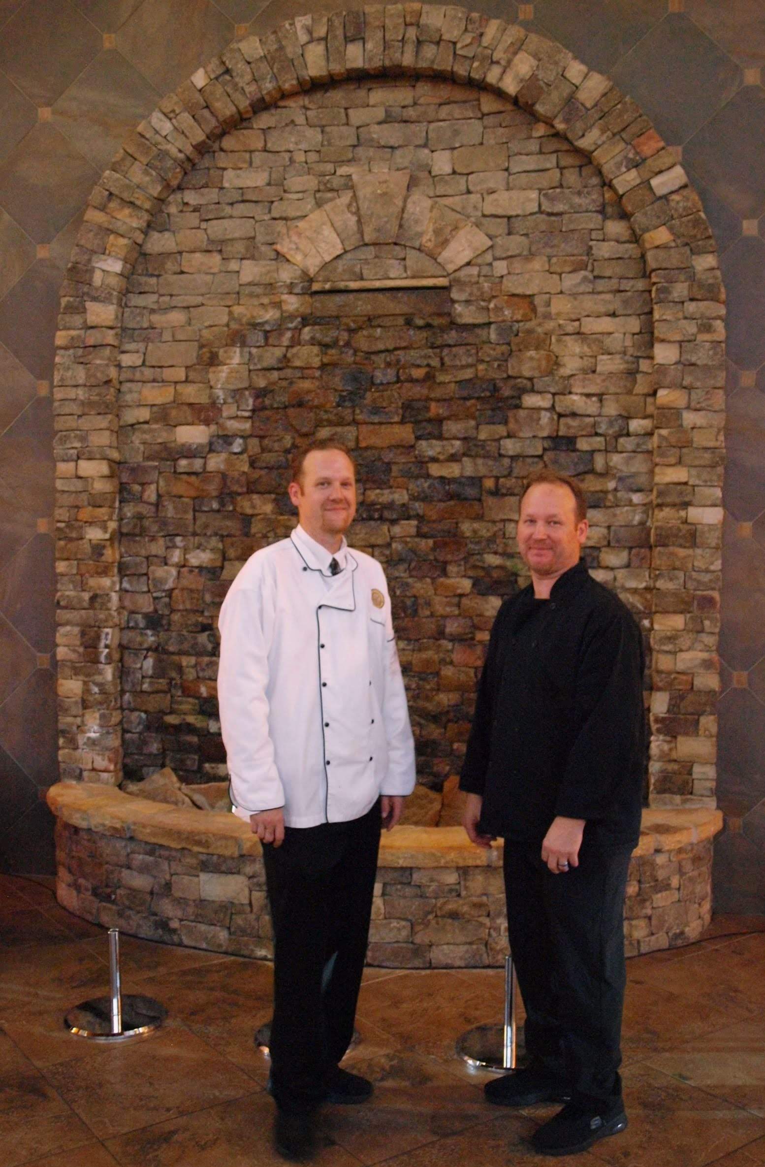 2 male caterers standing in front of stone wall