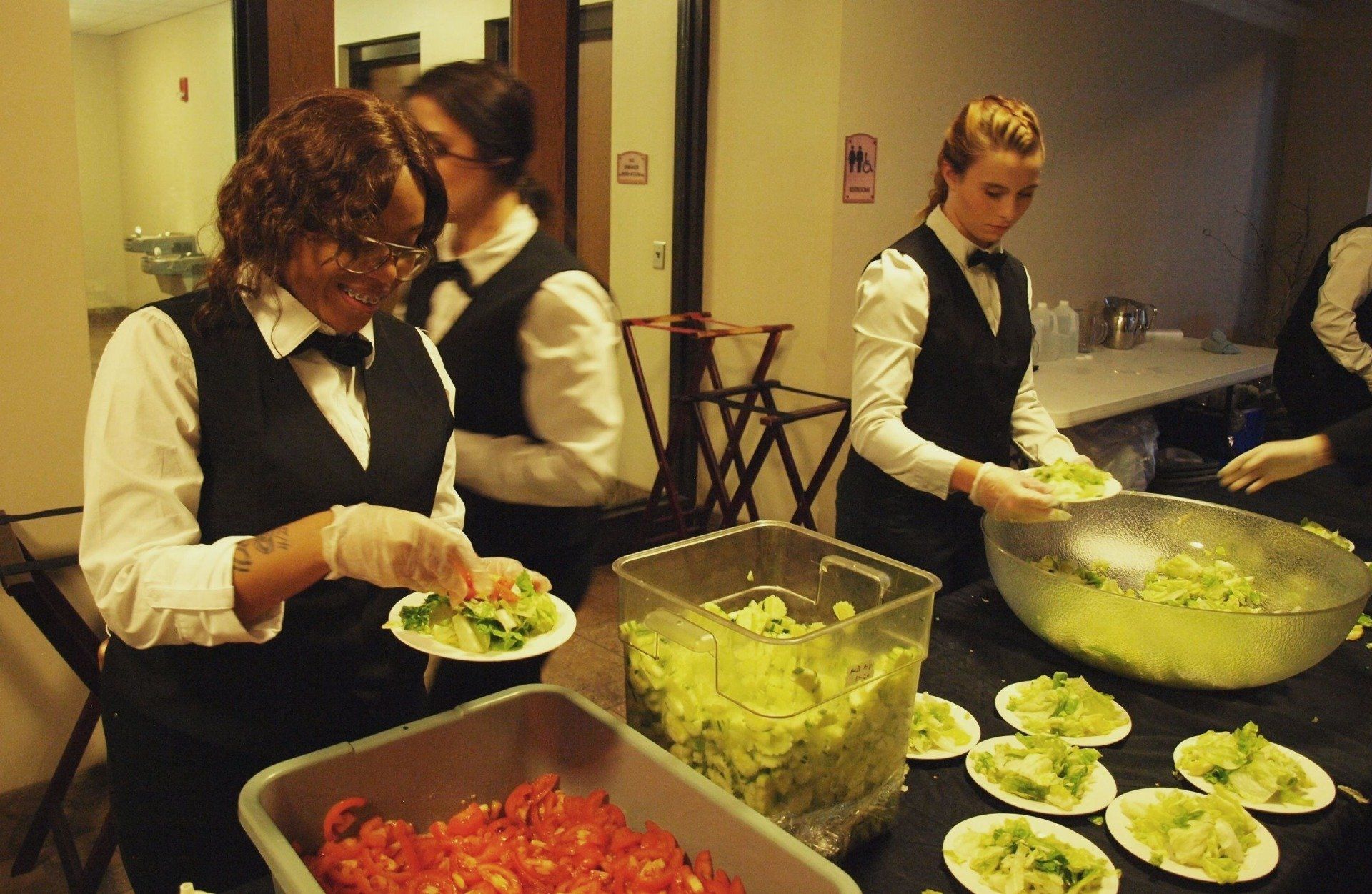 2 female caterers plating salad in buffet line