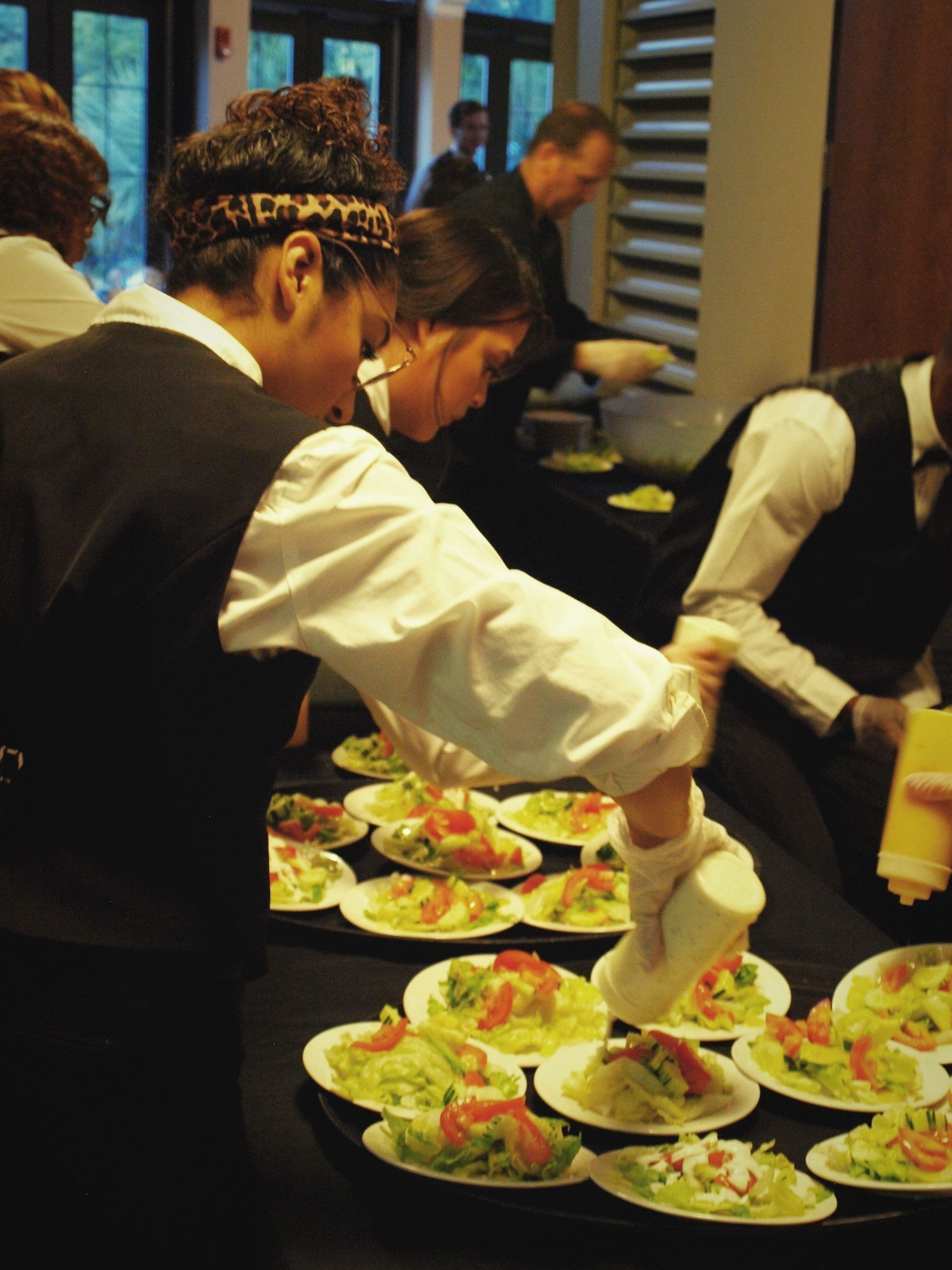 caterers putting dressing on plated salads