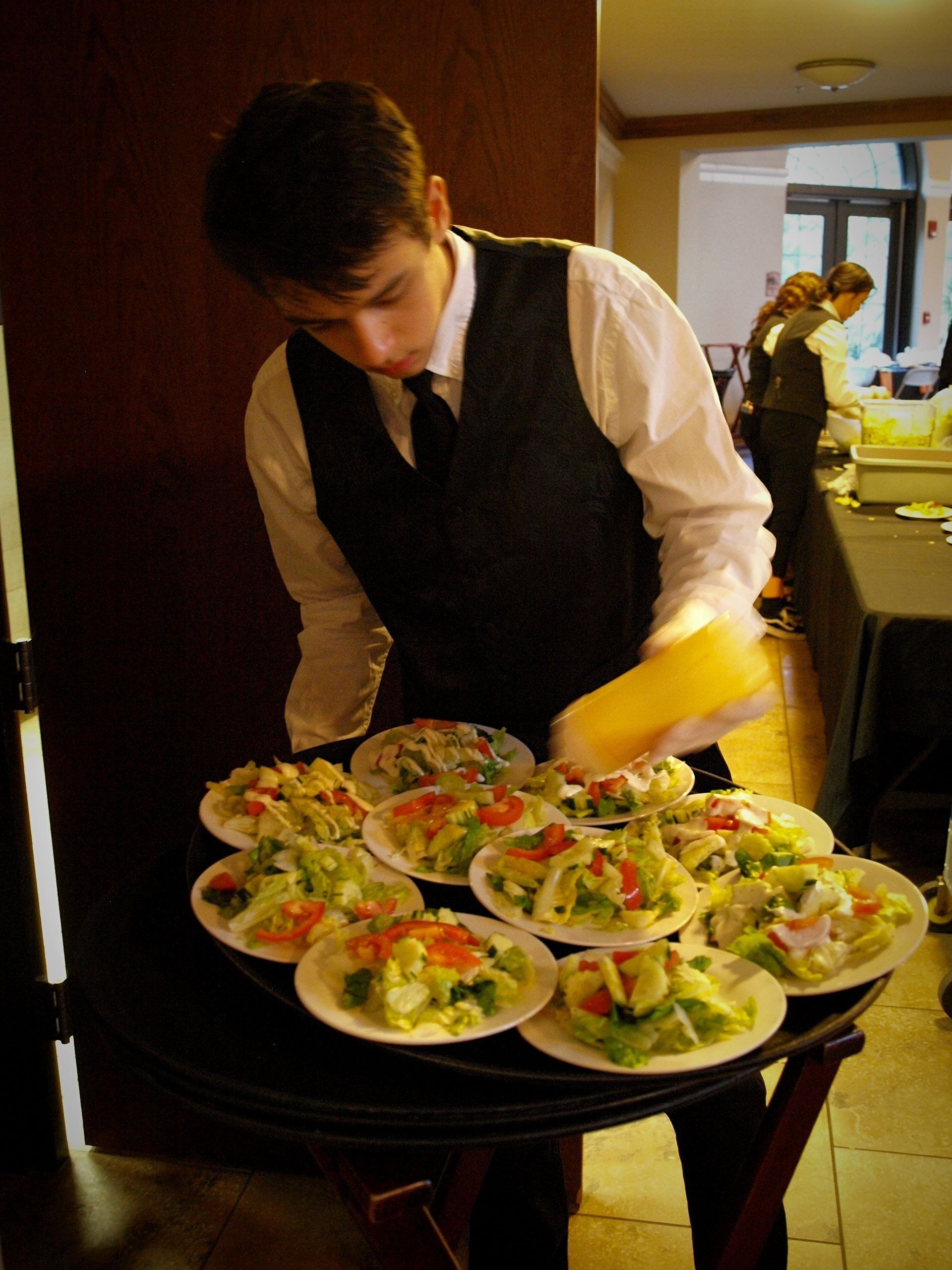 male caterer putting dressing on tray of salads