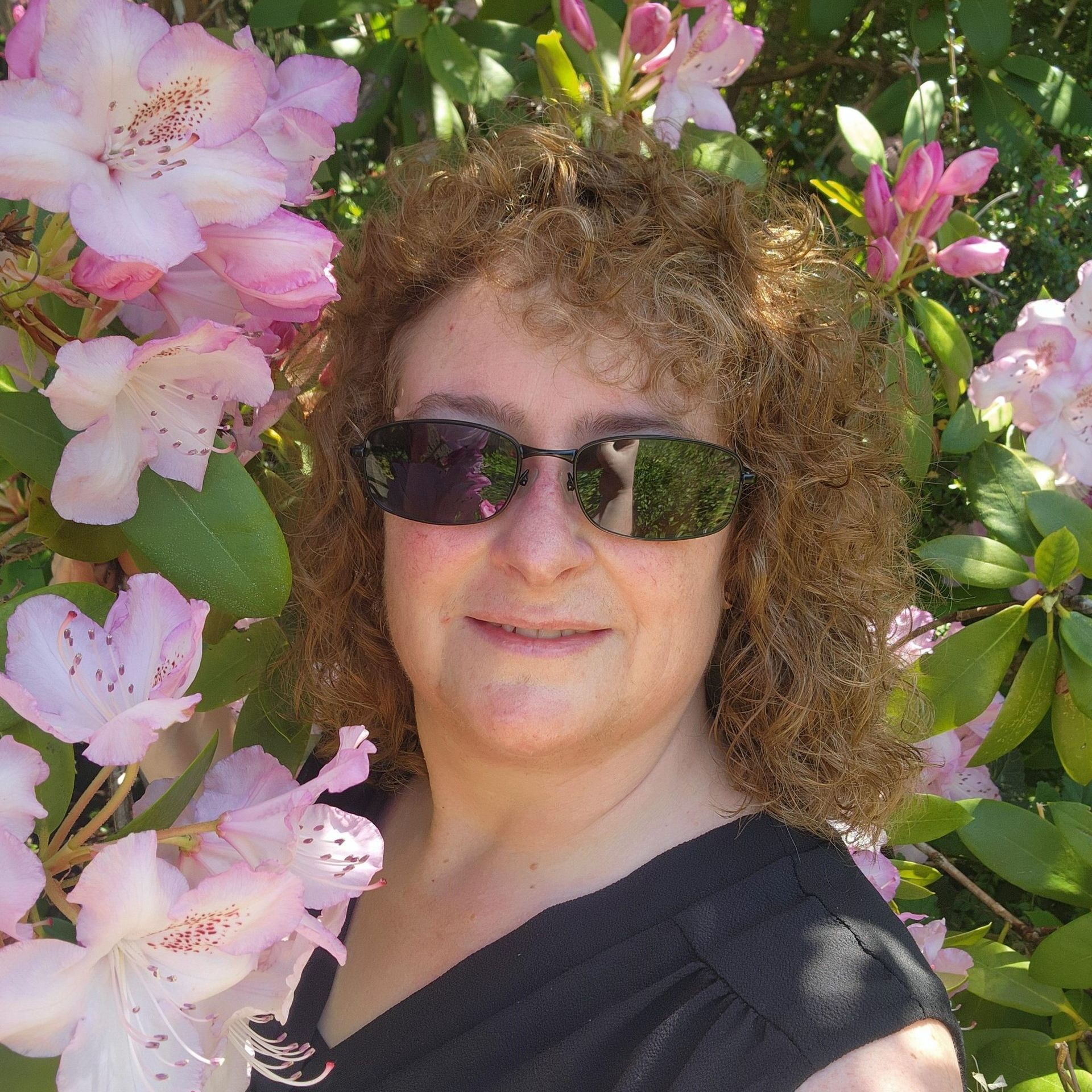 A woman with curly hair is wearing a purple jacket and smiling.