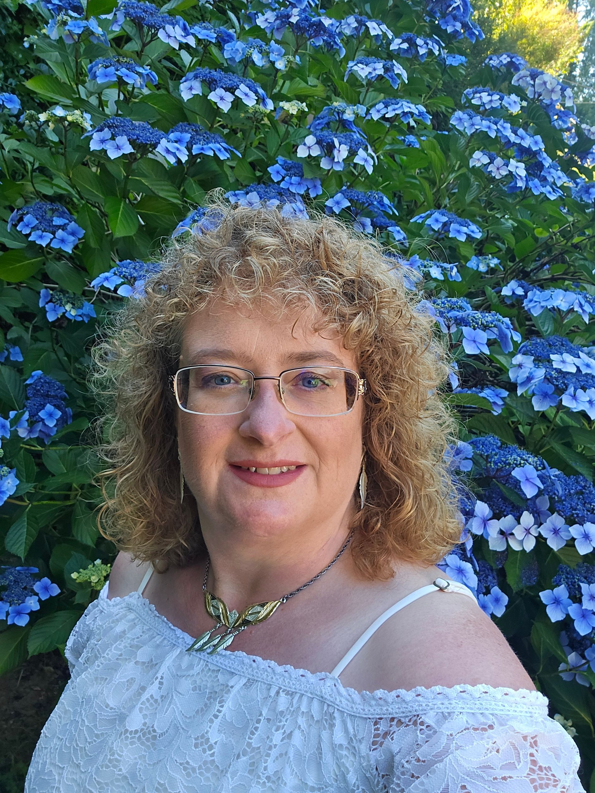 A woman with curly hair is wearing a purple jacket and smiling.