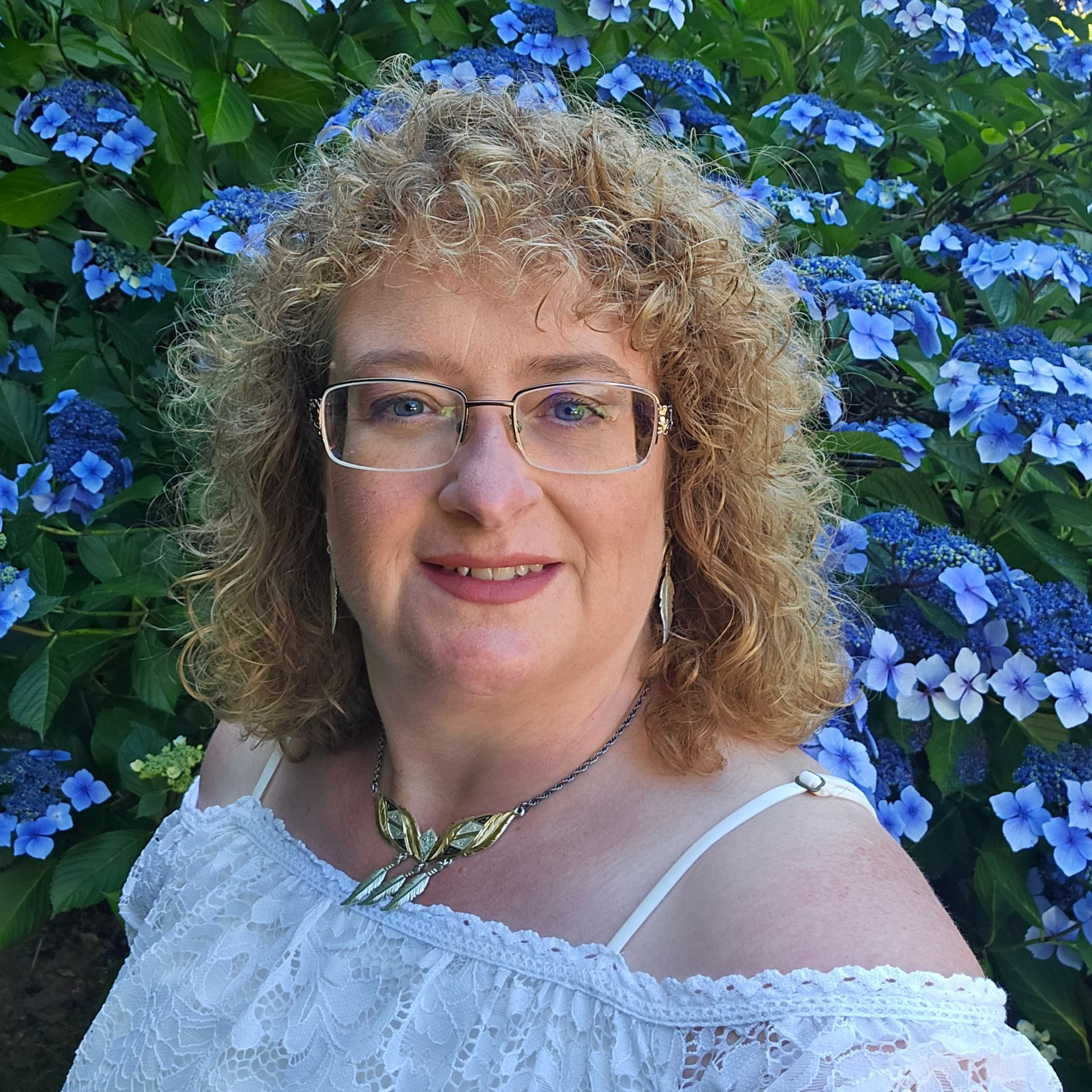 A woman with curly hair is wearing a purple jacket and smiling.
