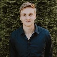 A young man in a black shirt is standing in front of a tree.