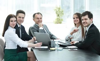 A group of business people are sitting around a table with laptops.