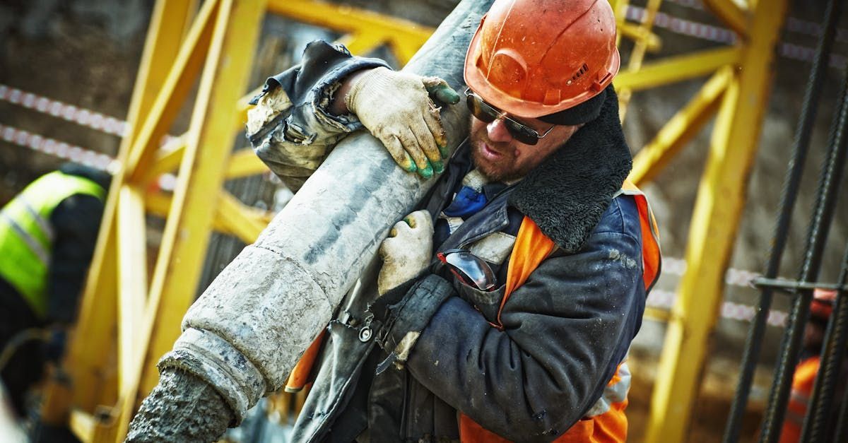 A construction worker is carrying a large pipe on his shoulders.