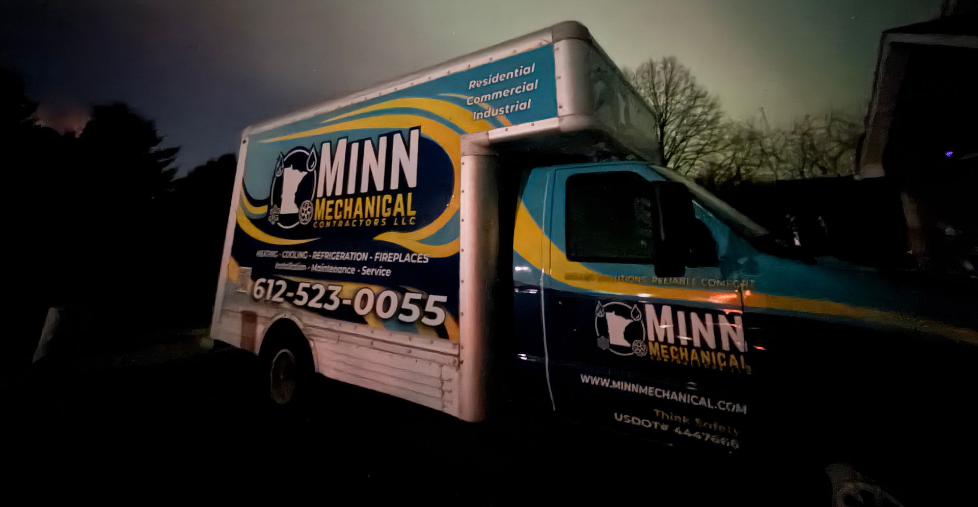 Blue and white Minn Mechanical service truck parked outside at night; company logo and phone number visible.